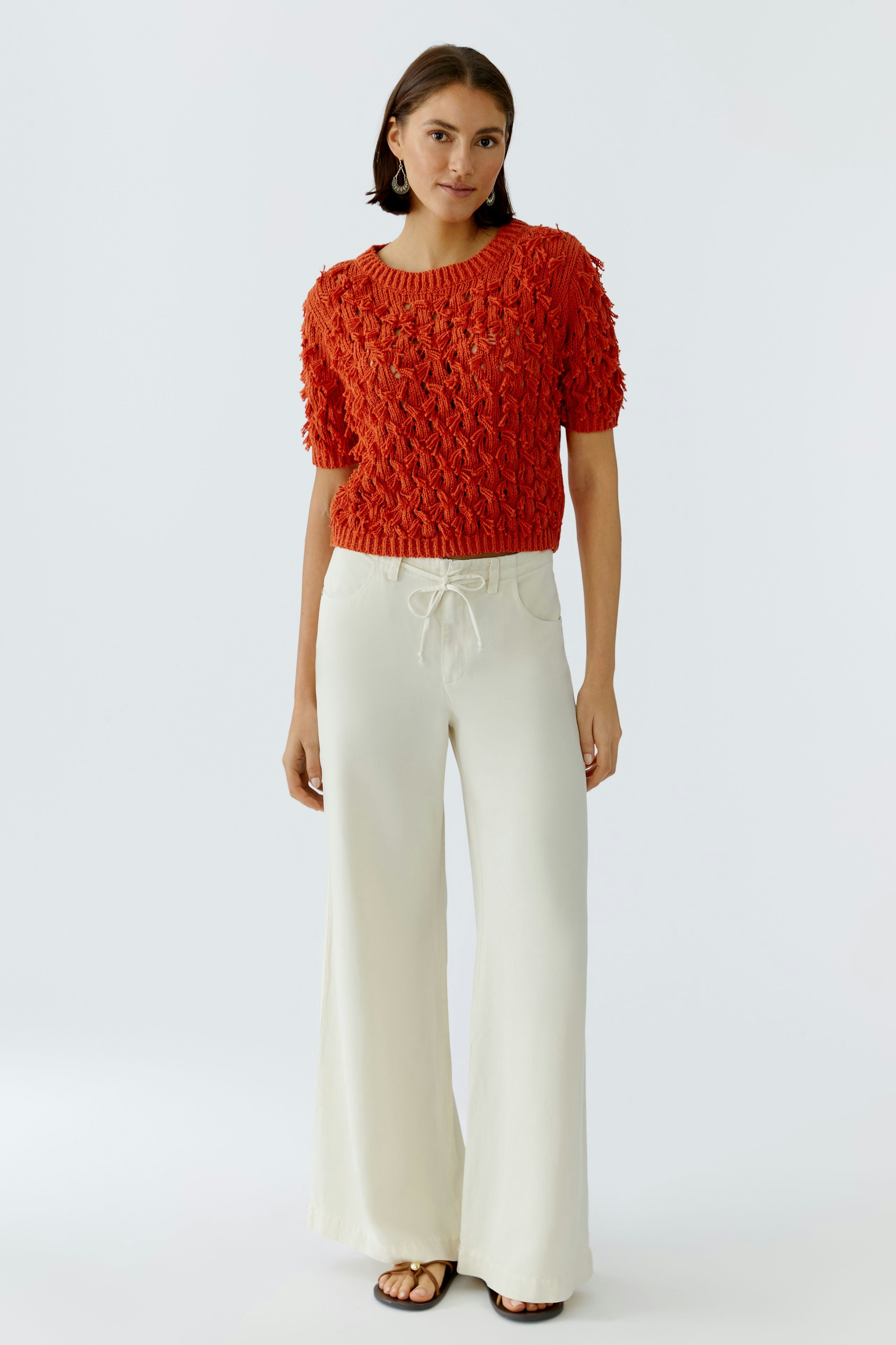 Damen-Pullover: Frau in rotem, strukturiertem Pullover mit kurzen Ärmeln und lässiger Hose.