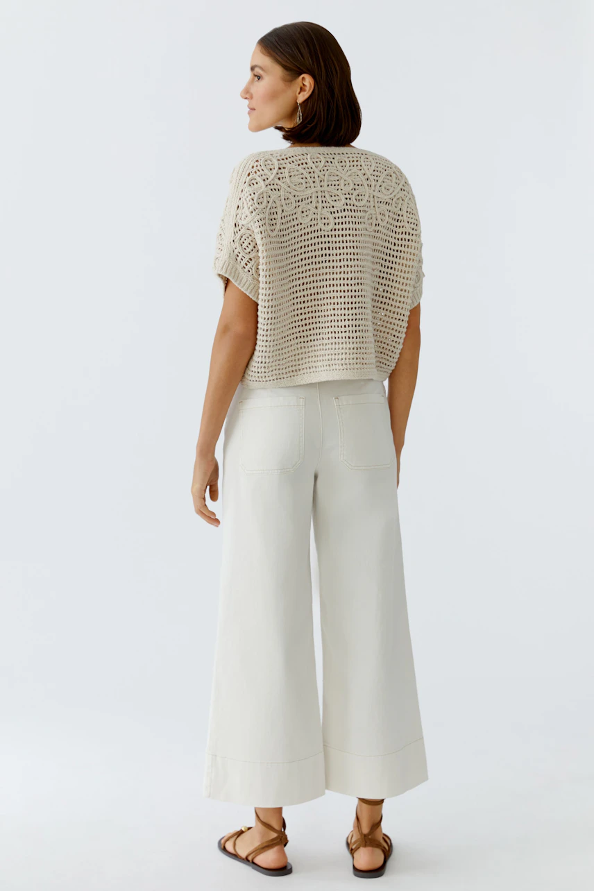 Casual women's pullover: A woman in a light crochet pullover, paired with wide-leg pants, seen from the back.
