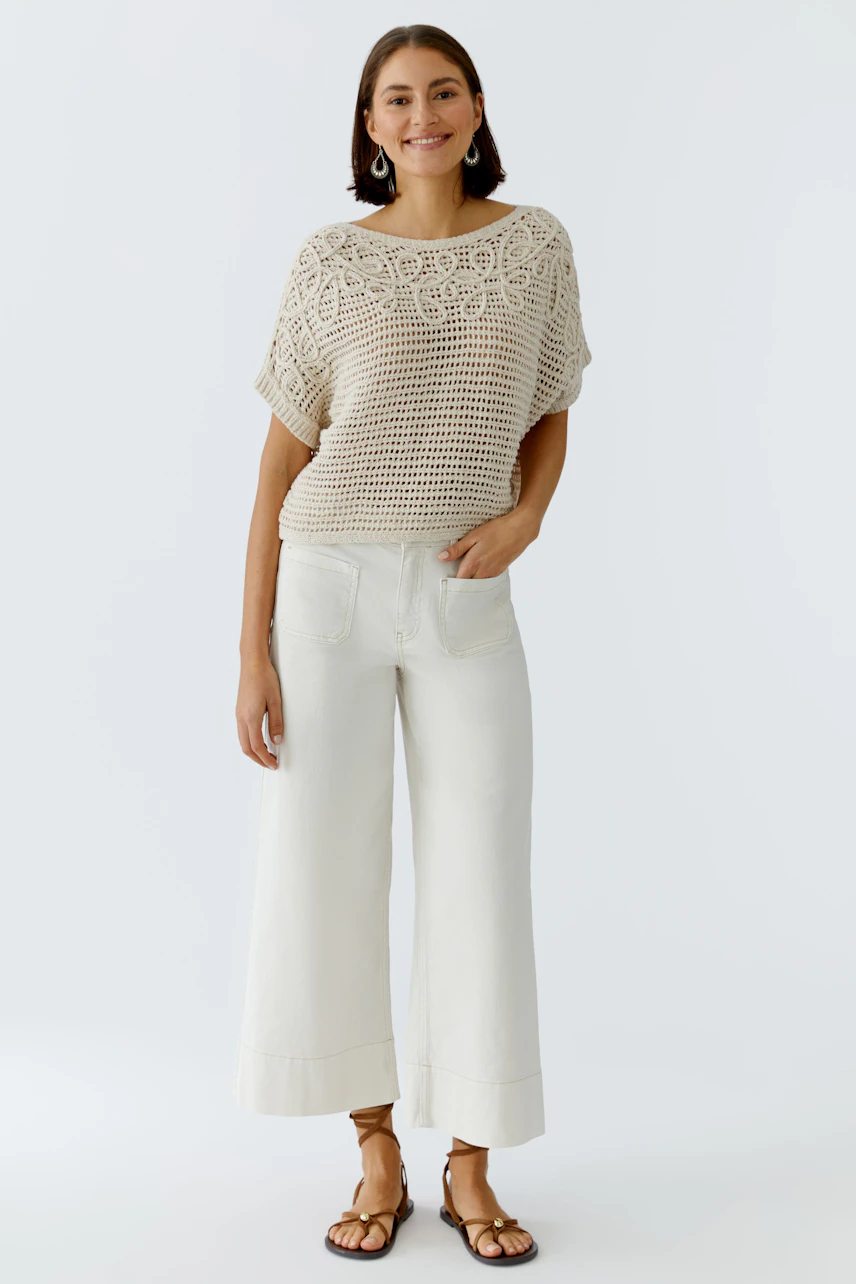 Casual women's pullover: Smiling woman in a light crochet pullover paired with wide white pants.