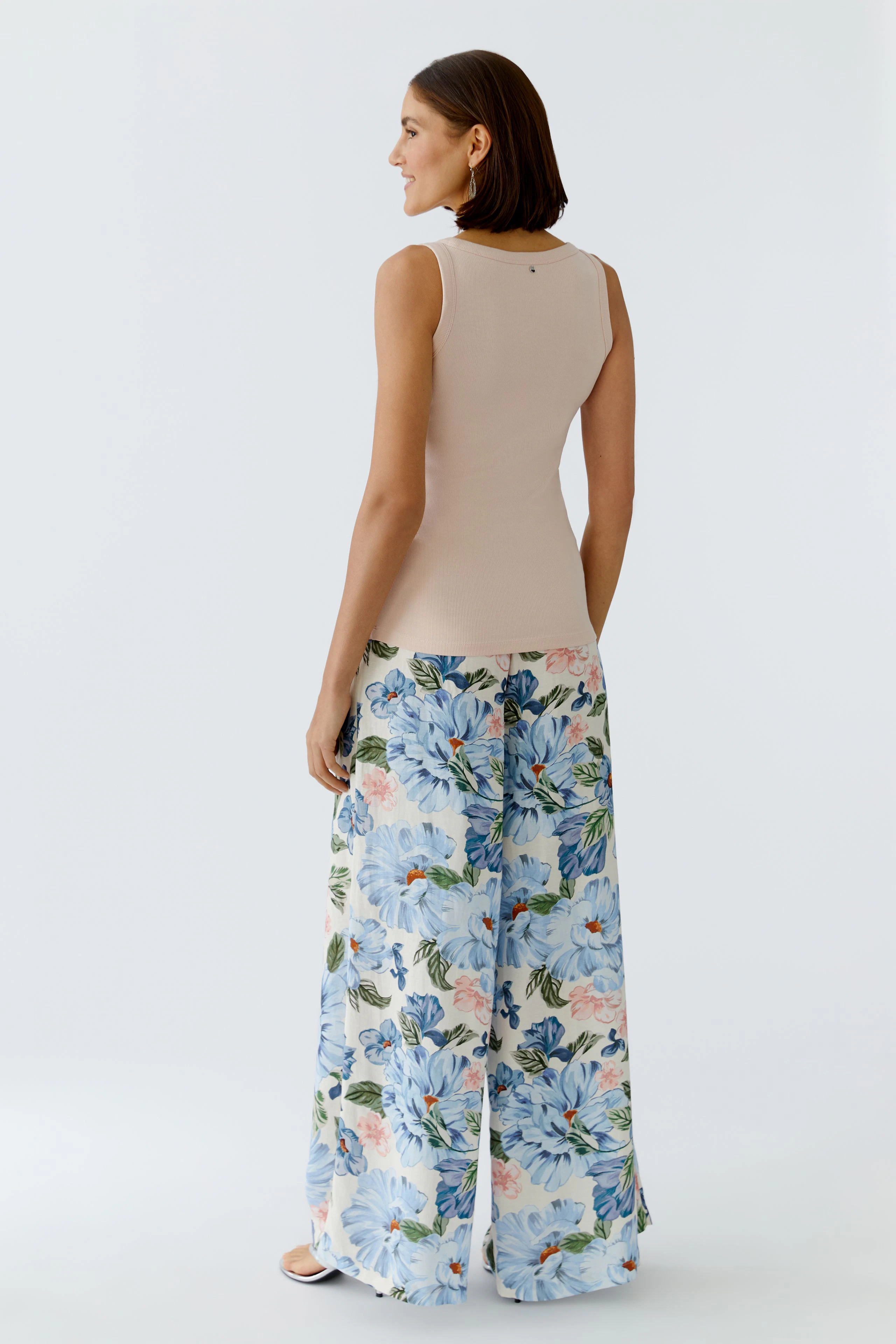 Casual women's tank top: A woman in a fitted beige tank top paired with floral wide-leg pants.