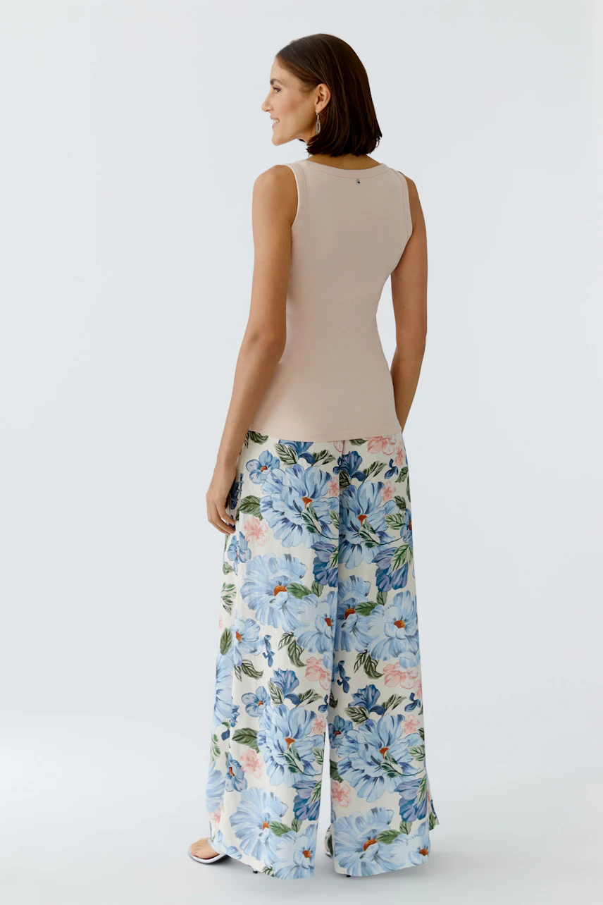 Casual women's tank top: A woman in a fitted beige tank top paired with floral wide-leg pants.