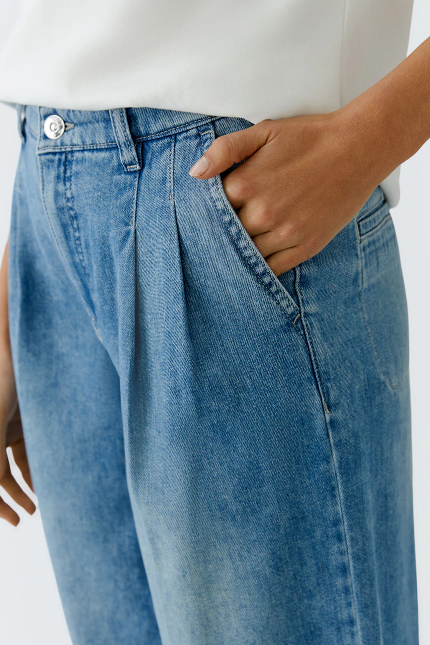 Casual women's pleated trousers in light blue denim, featuring side pockets and a relaxed fit.