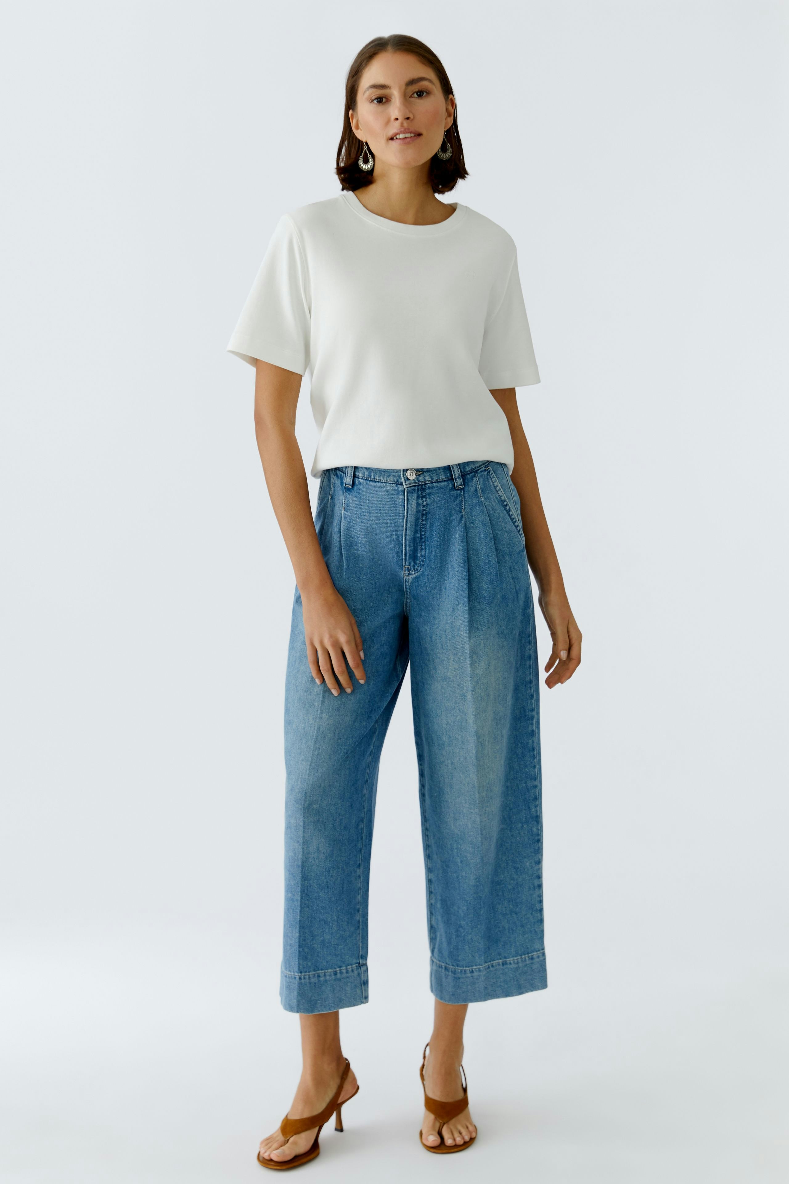 Bequeme Bundfaltenhose: Frau in lässiger Hose mit weitem Schnitt und hellem Oberteil steht entspannt.