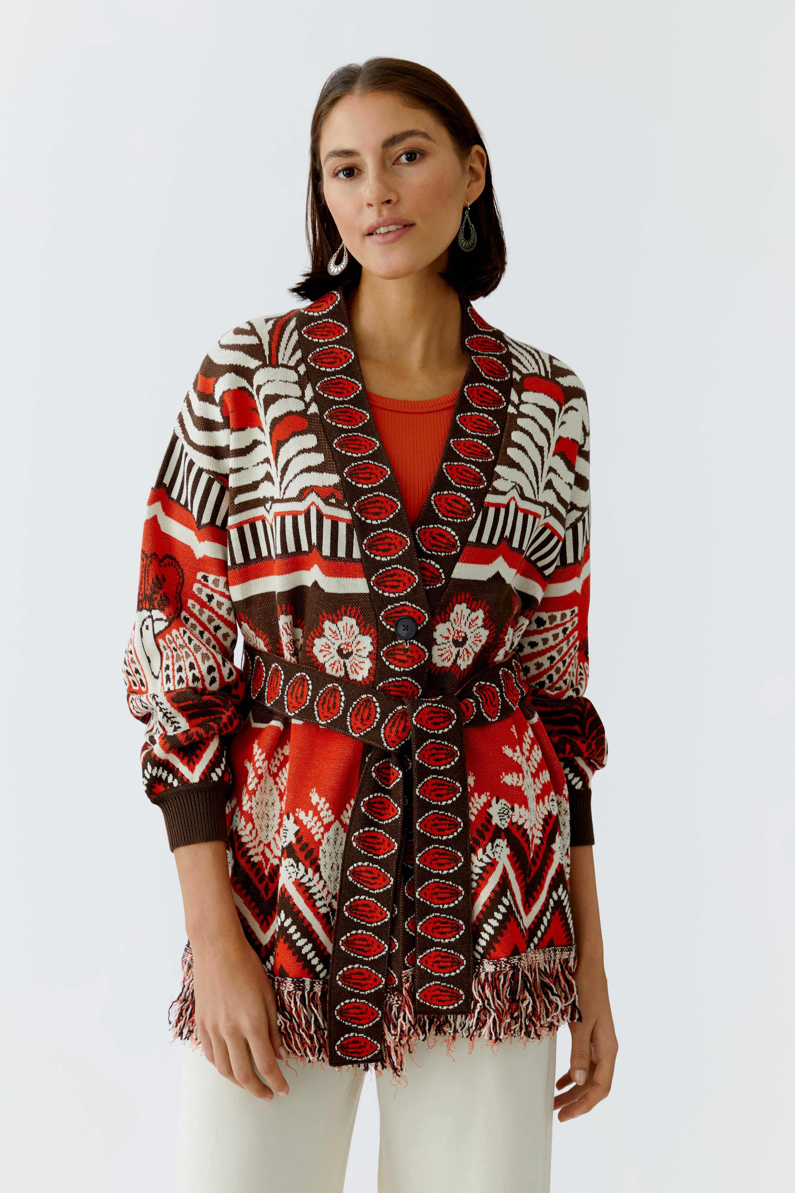 Colorful women's cardigan with a patterned design and fringe details, worn over a red top.