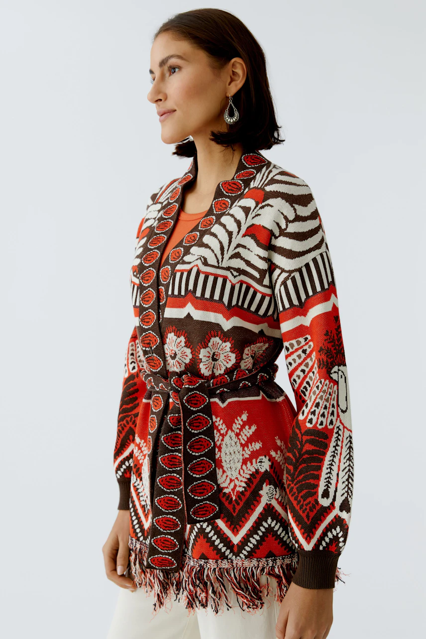 Colorful women's cardigan with a unique pattern and fringe details, styled with a belt.