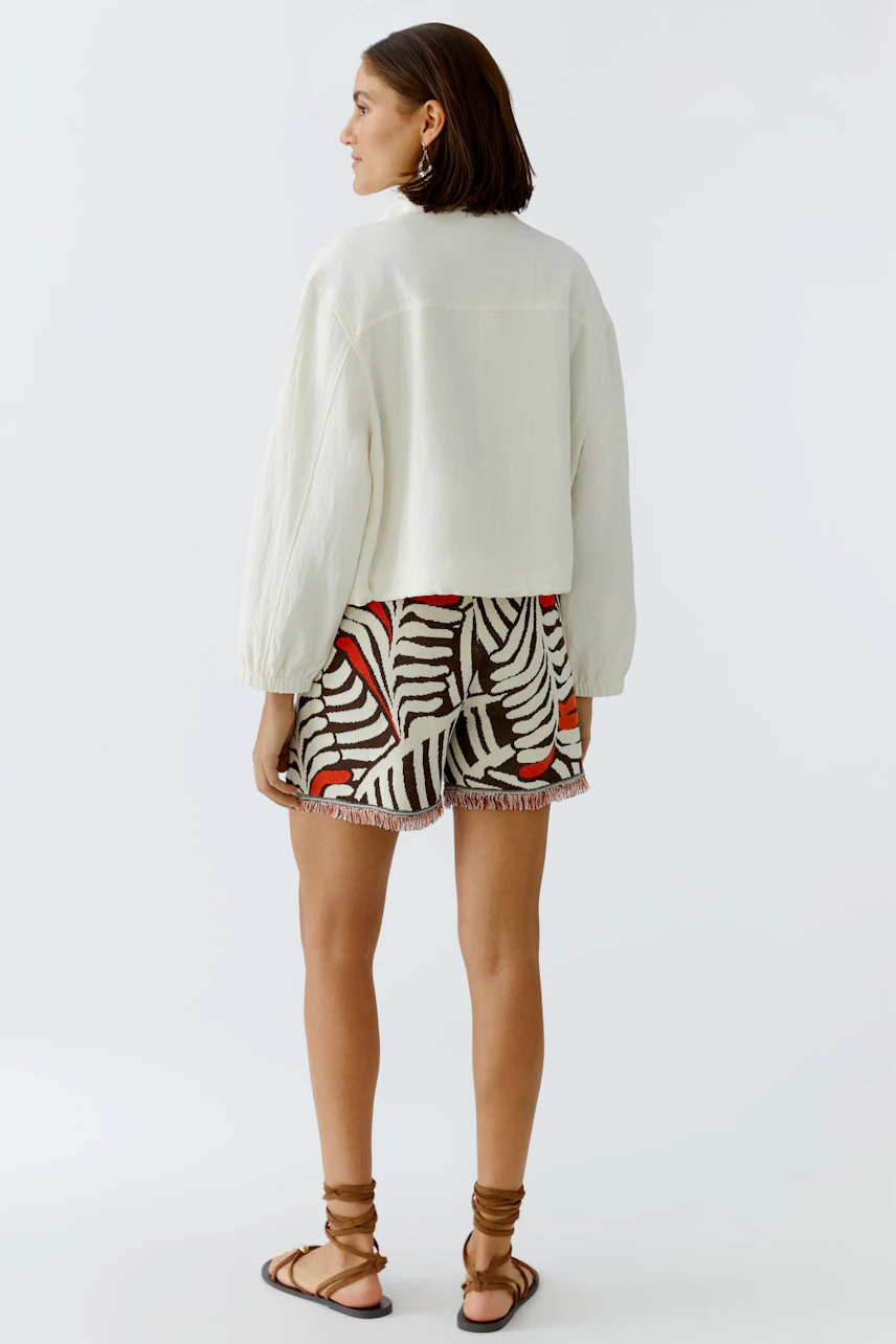 Casual women's blouson: A woman in a light jacket paired with patterned shorts, showcasing a relaxed style.