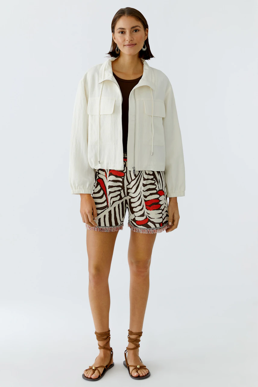 Casual women's blouson: A woman in a light jacket over a brown top and patterned shorts.