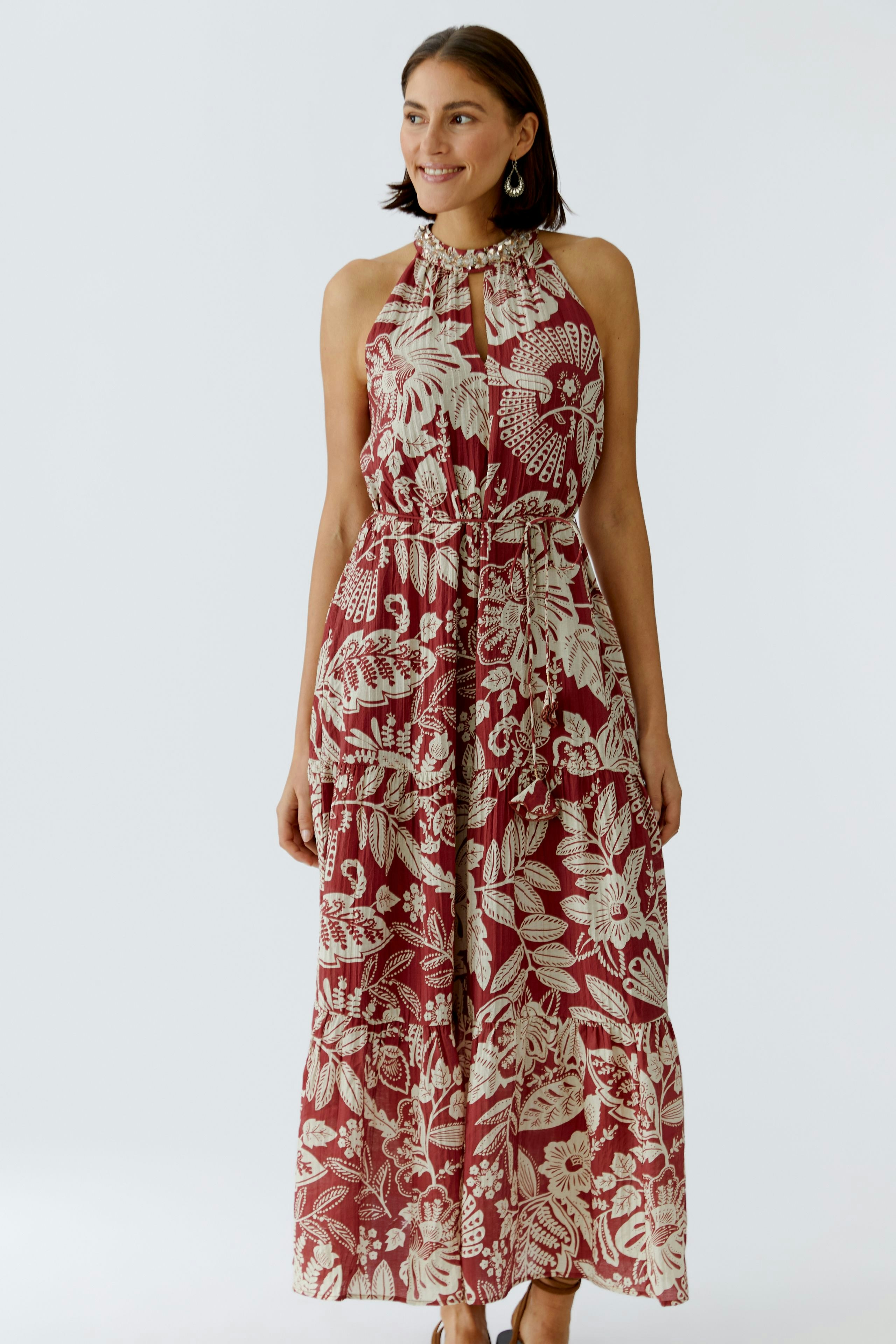 Maxikleid: Frau in einem blumigen, ärmellosen Maxikleid mit Bindegürtel und Rüschendetails.