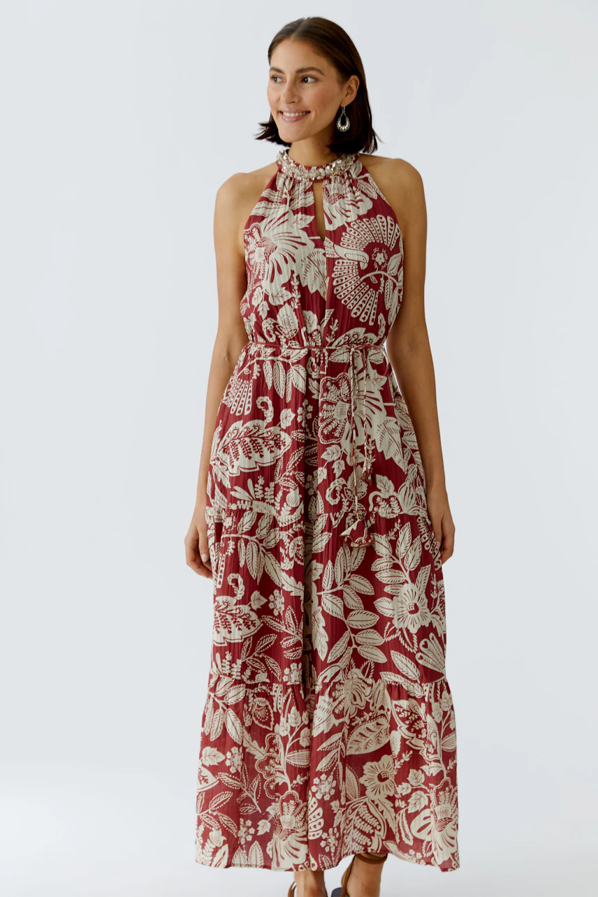Maxikleid: Frau in einem blumigen, ärmellosen Maxikleid mit Bindegürtel und Rüschendetails.