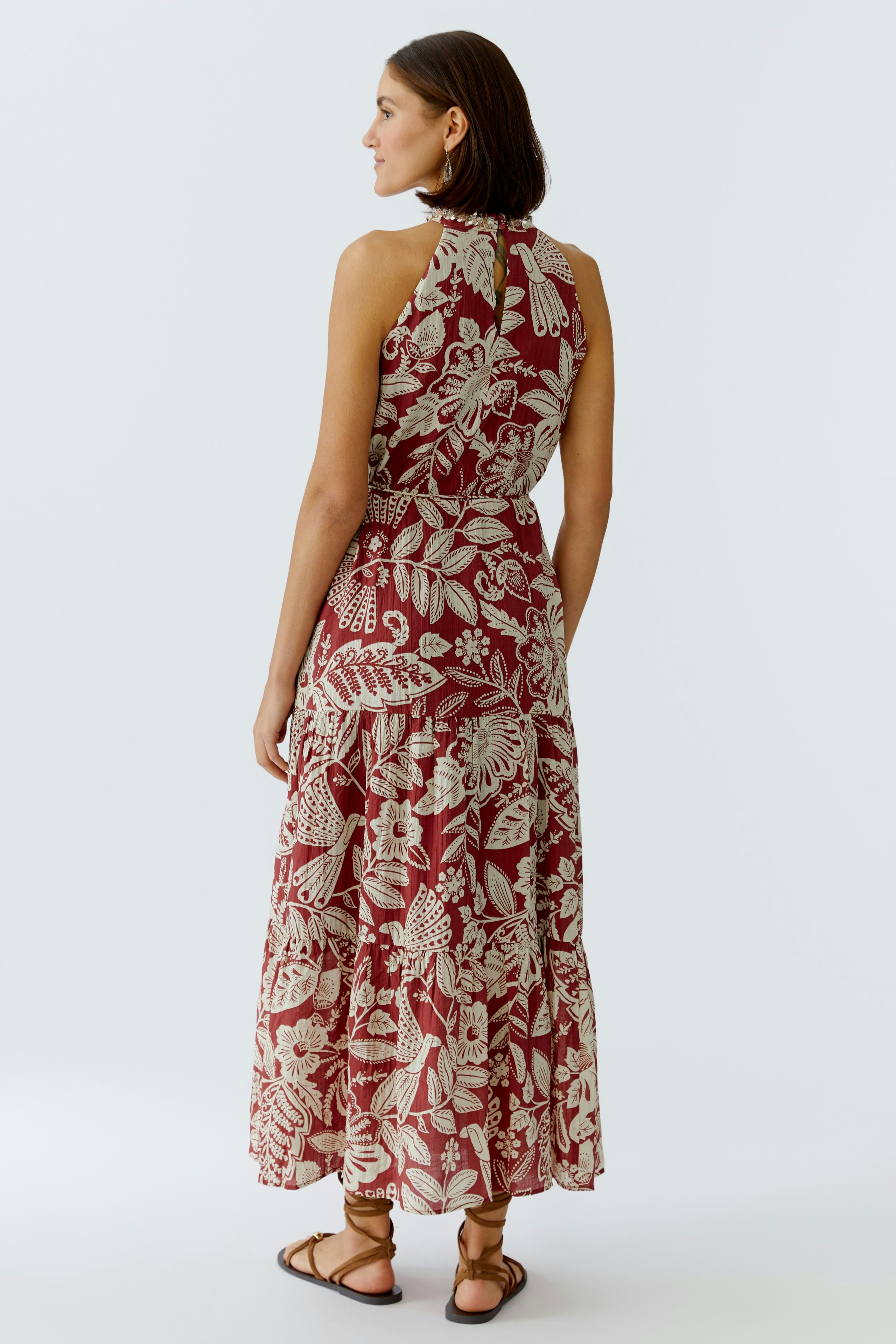 Maxikleid: Frau in einem rot-blumigen Maxikleid mit lockerer Passform und Sandalen von hinten.