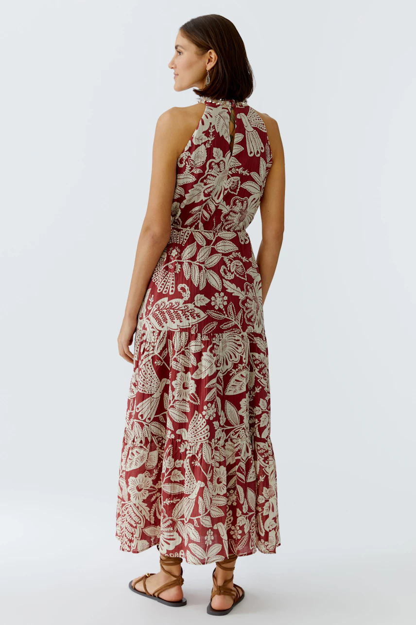 Maxikleid: Frau in einem rot-blumigen Maxikleid mit lockerer Passform und Sandalen von hinten.