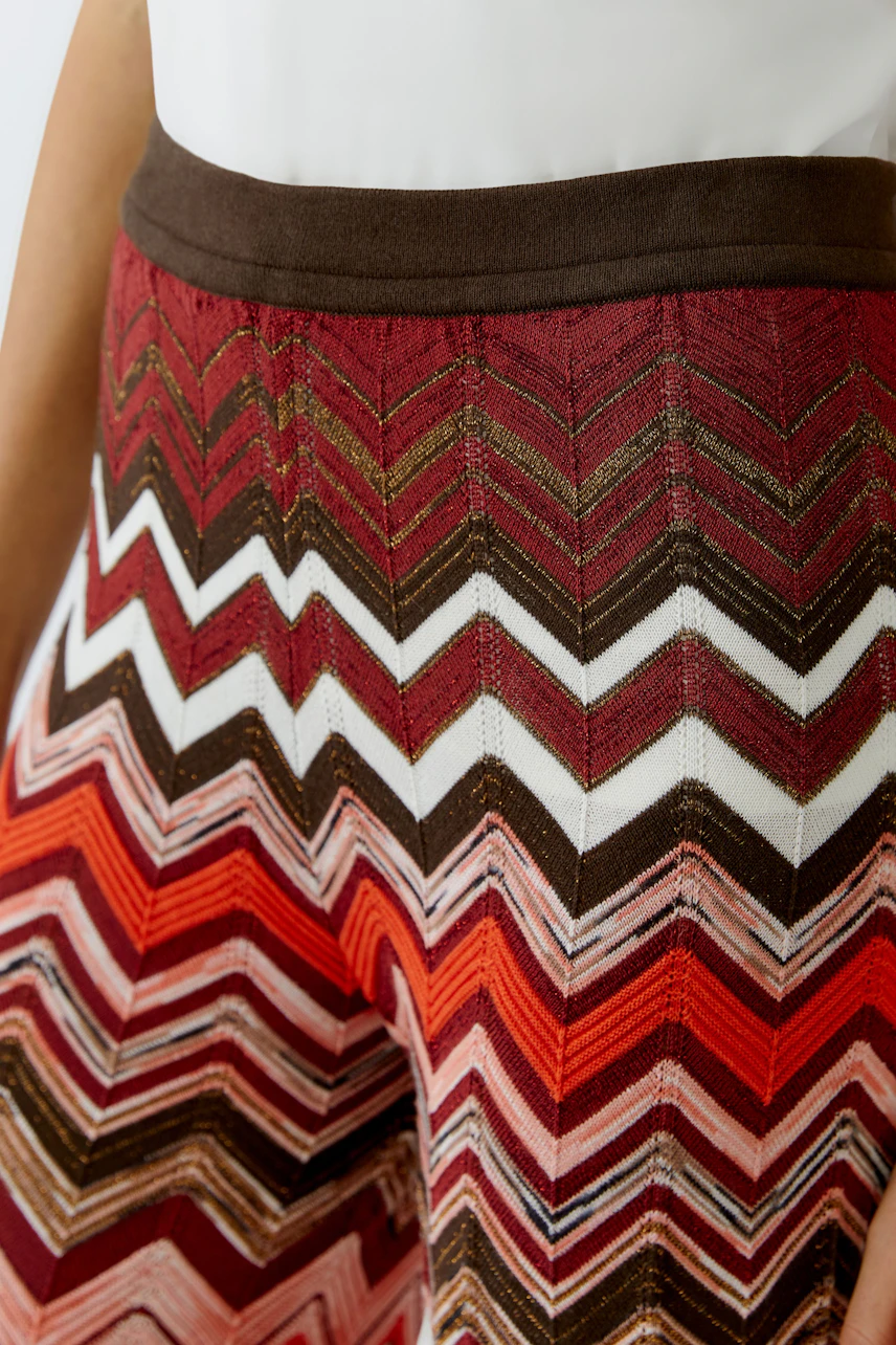 Colorful knit pants with zigzag pattern in red, brown, and white. Close-up of fabric texture.
