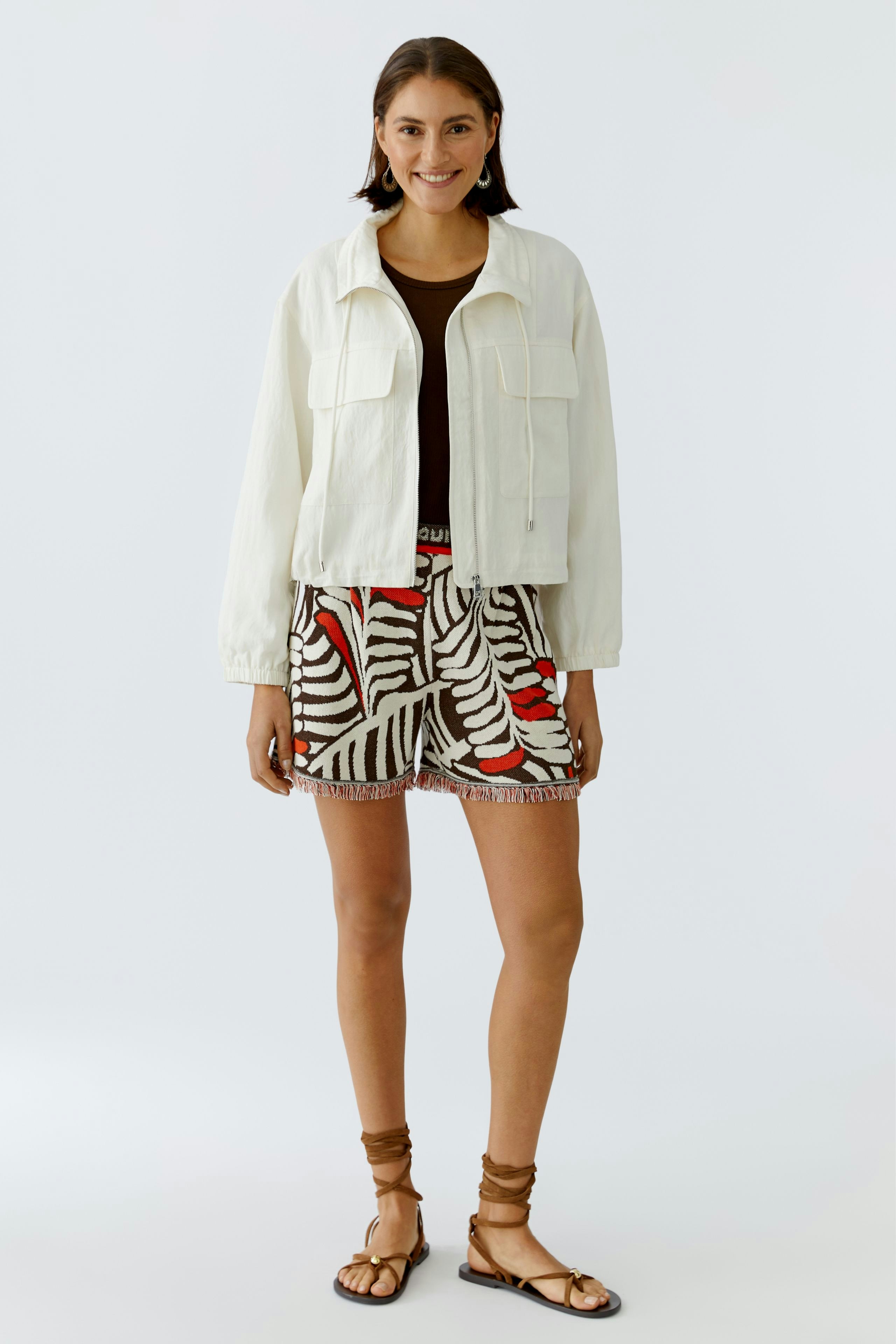 Bequeme Damen-Shorts mit buntem Blattmuster, kombiniert mit einer lässigen Jacke und Sandalen.