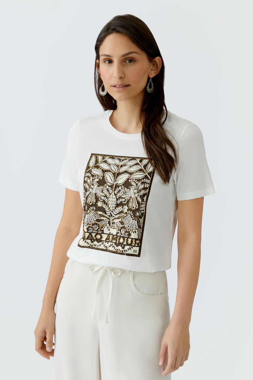 Casual women's T-shirt: Woman in a white tee with a botanical print, paired with light pants.