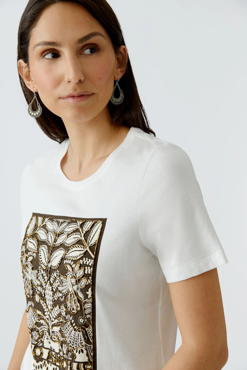 Casual women's T-shirt: Young woman in a white tee with a floral print, looking confidently.