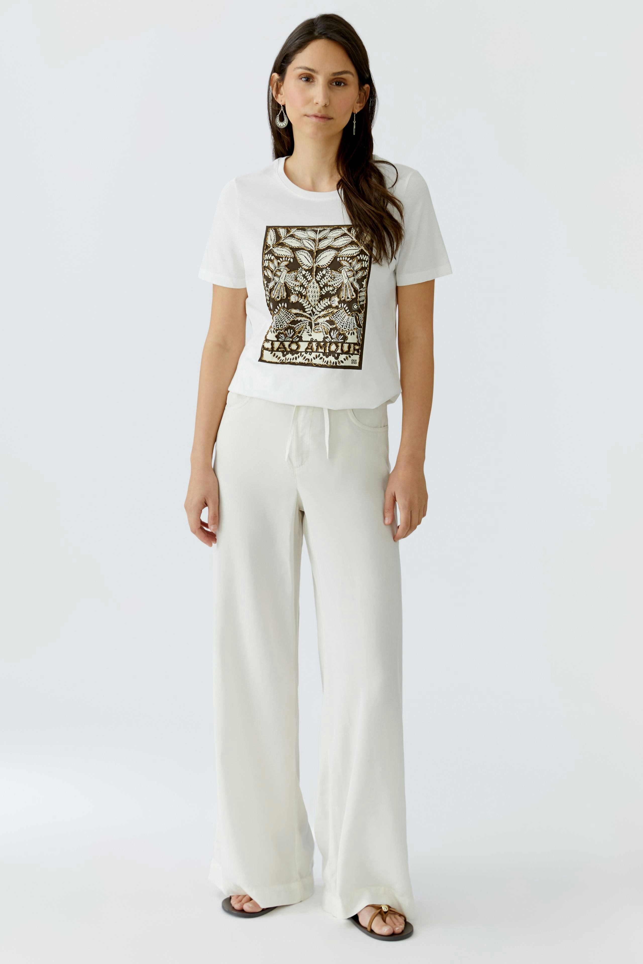 Damen-T-Shirt: Frau trägt ein weißes T-Shirt mit grafischem Print und lässigen, hellen Hosen.