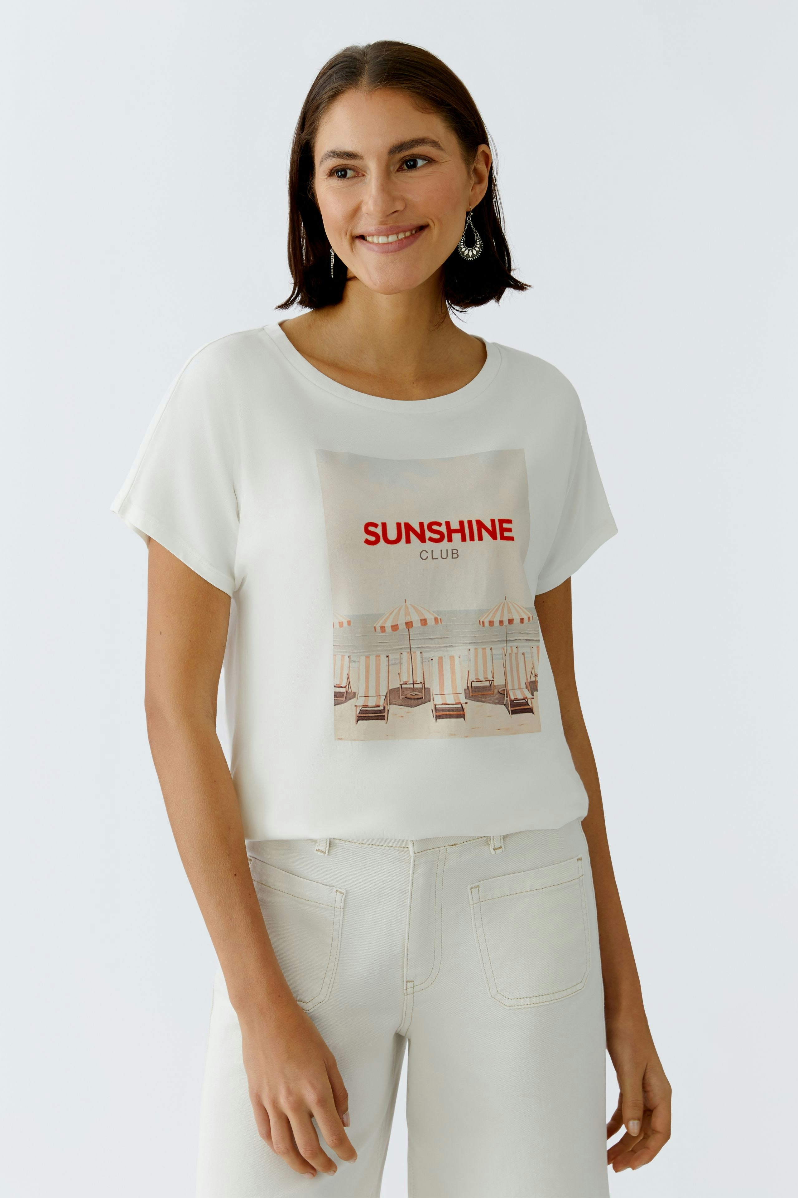 Damen-T-Shirt: Frau trägt ein weißes T-Shirt mit buntem Print und lässigem Schnitt.