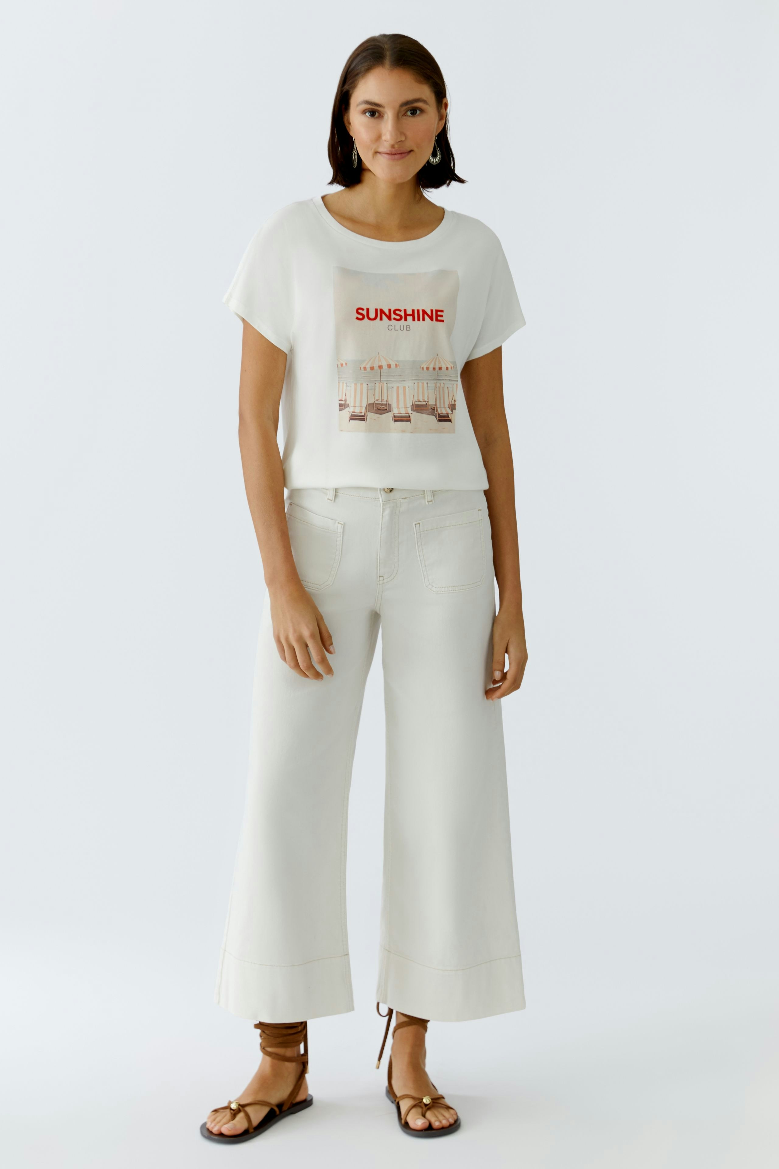 Bequemes Damen-T-Shirt: Frau trägt ein weißes T-Shirt mit buntem Print und lässigen, hellen Hosen.