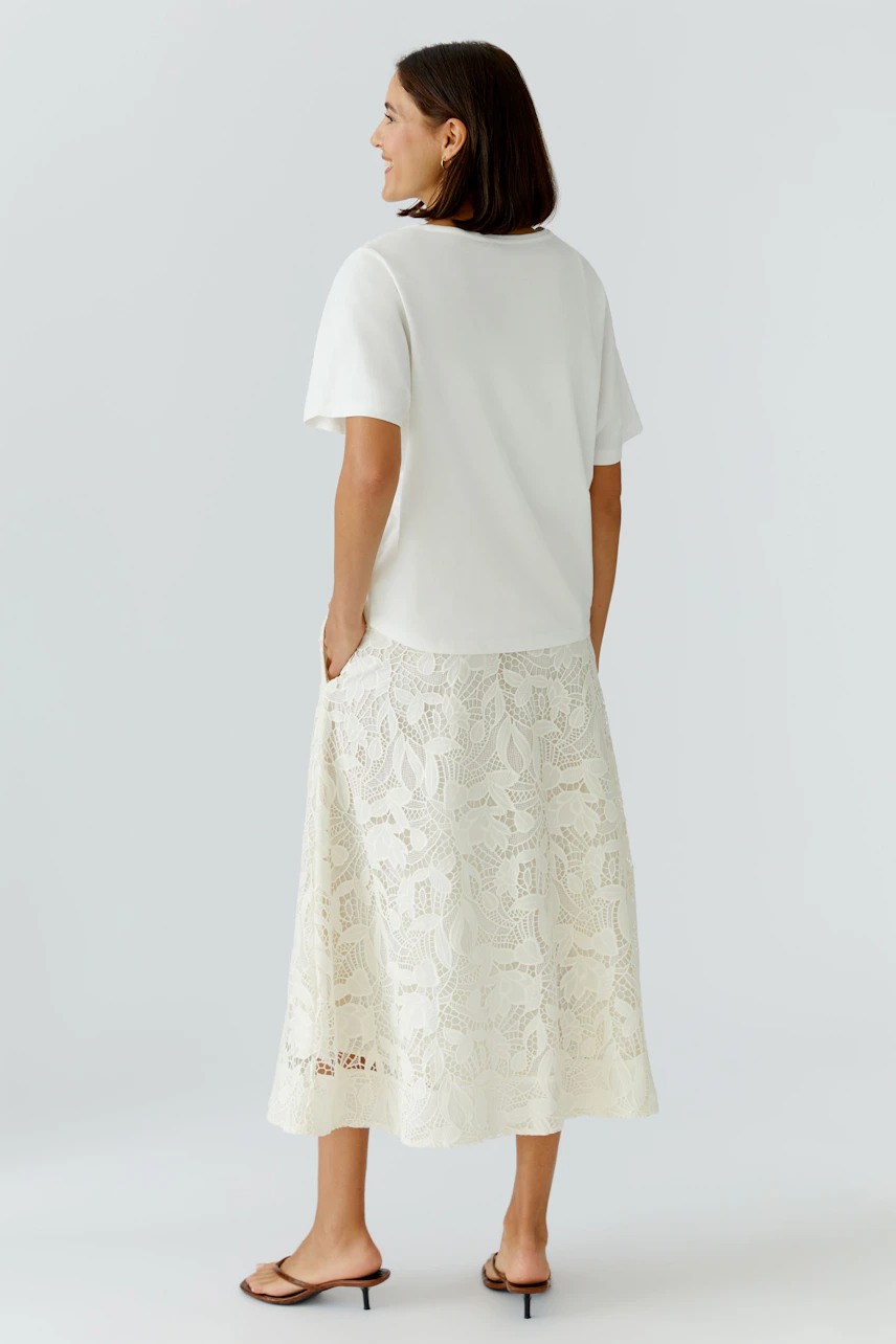 Casual women's T-shirt: Woman in a white short-sleeve top paired with a lace skirt, standing confidently.