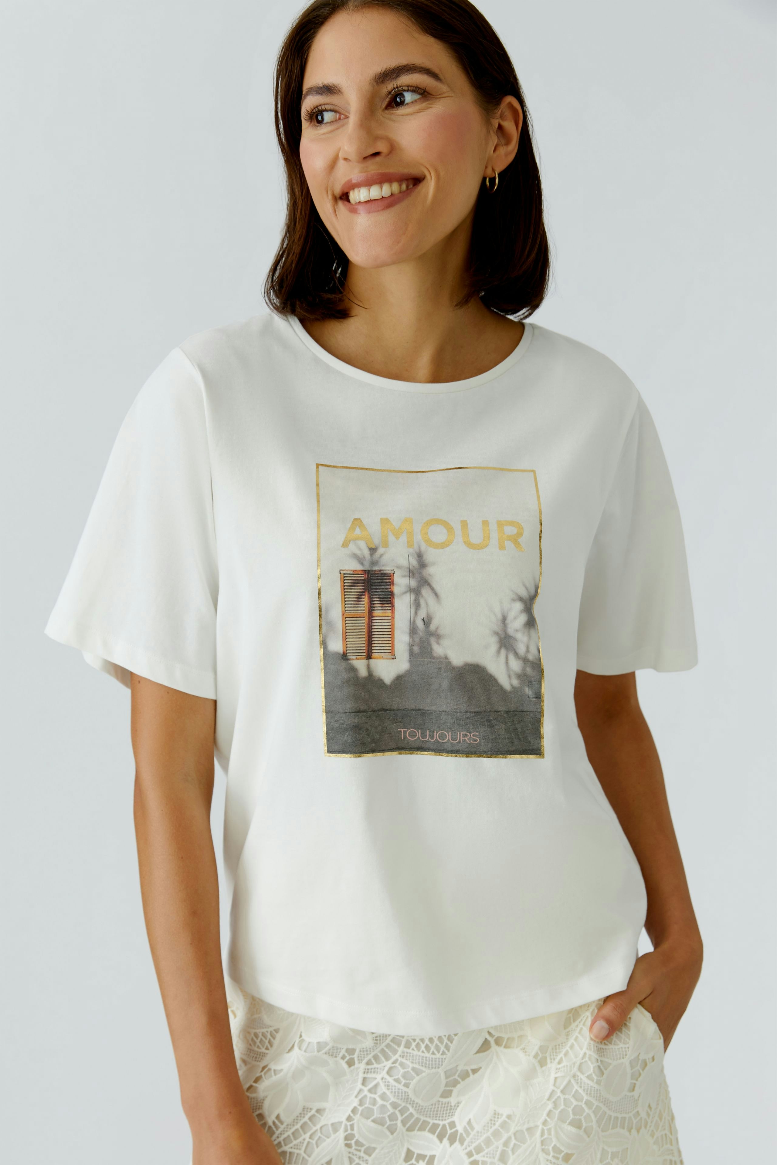 Bequemes Damen-T-Shirt: Frau lächelt in einem weißen Shirt mit grafischem Print und lässigem Schnitt.