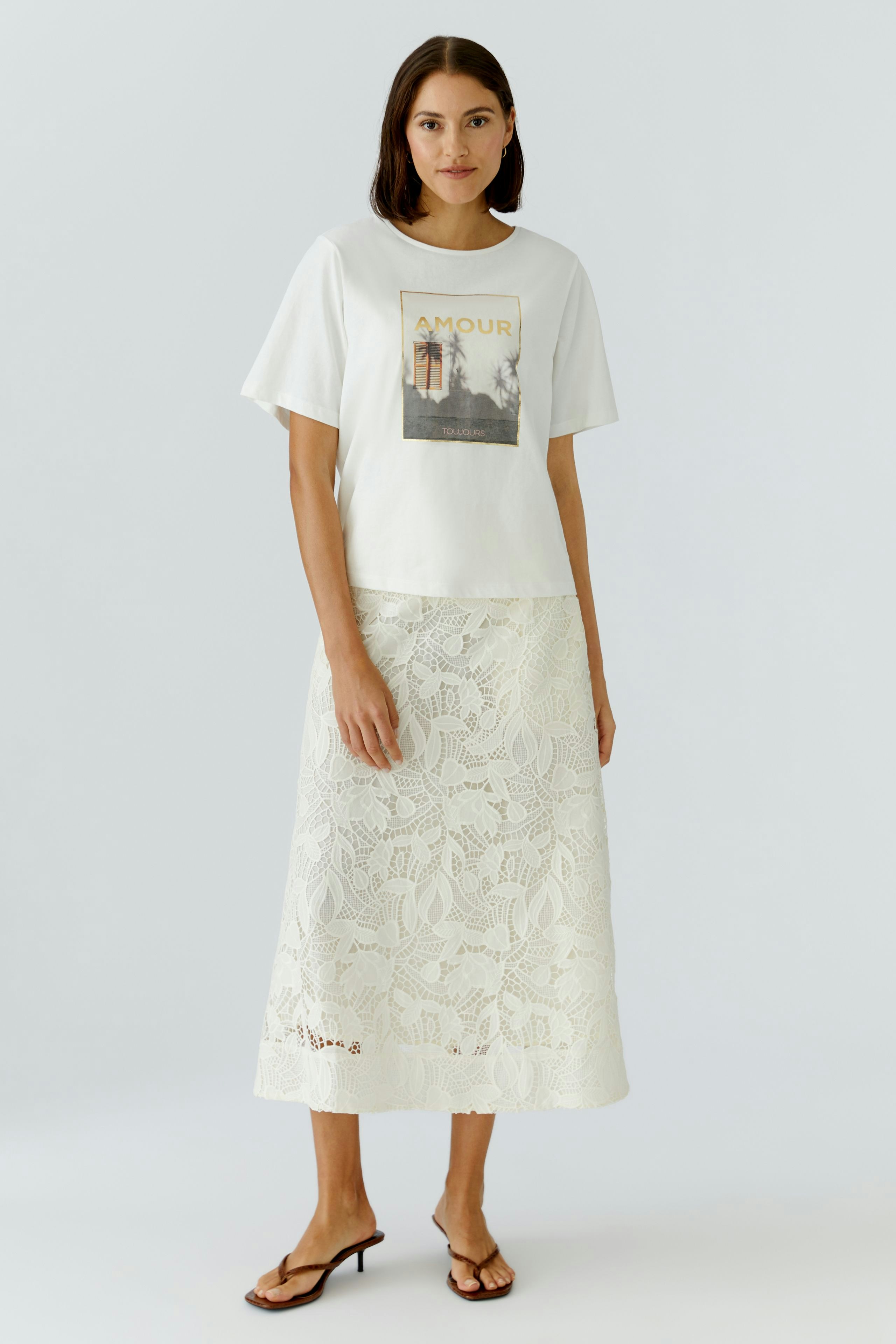 Damen-T-Shirt: Frau trägt ein weißes T-Shirt mit Aufdruck und kombiniert es mit einem hellen Rock.