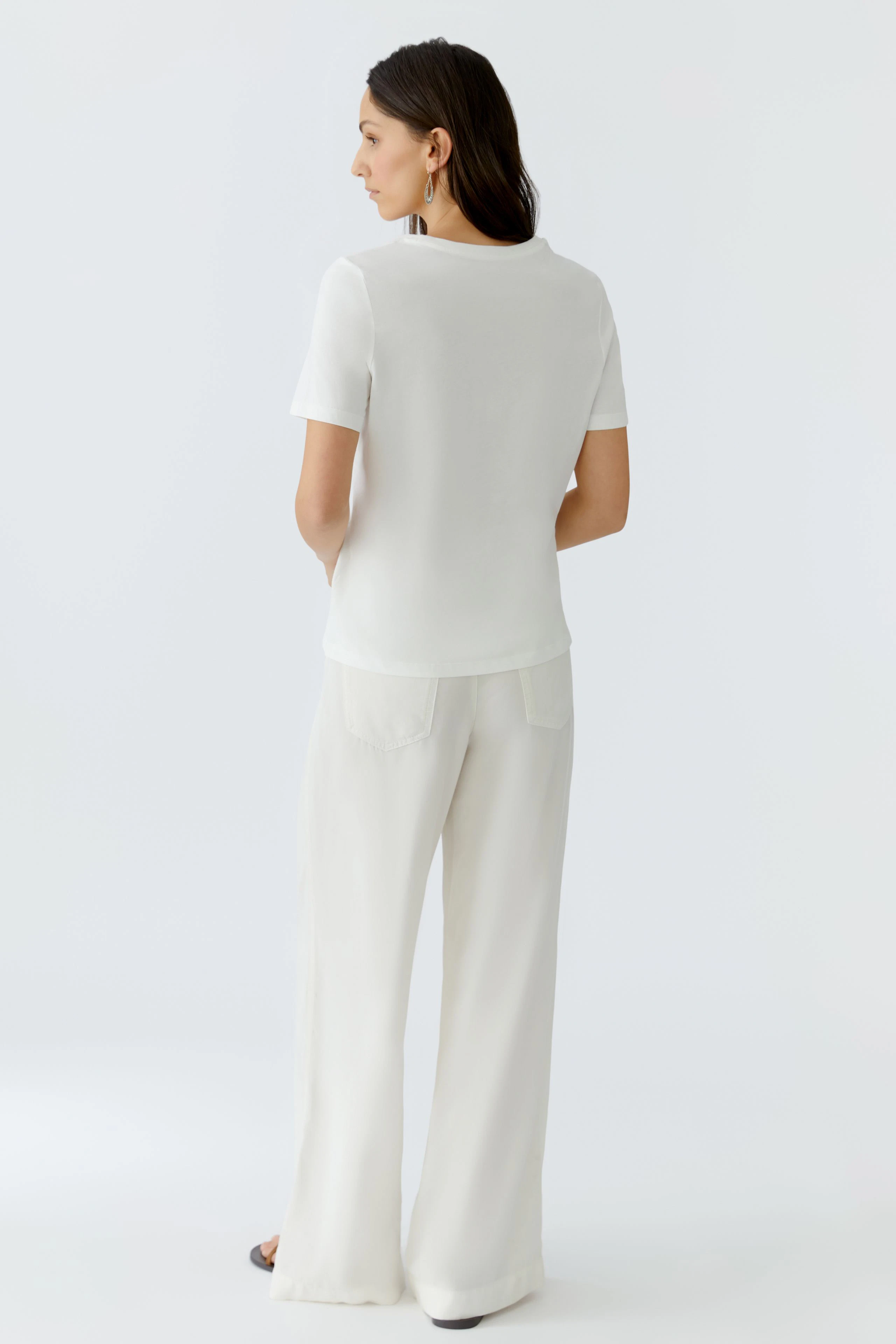 Damen-T-Shirt: Frau in weißem T-Shirt mit kurzen Ärmeln und lässiger Hose von hinten.