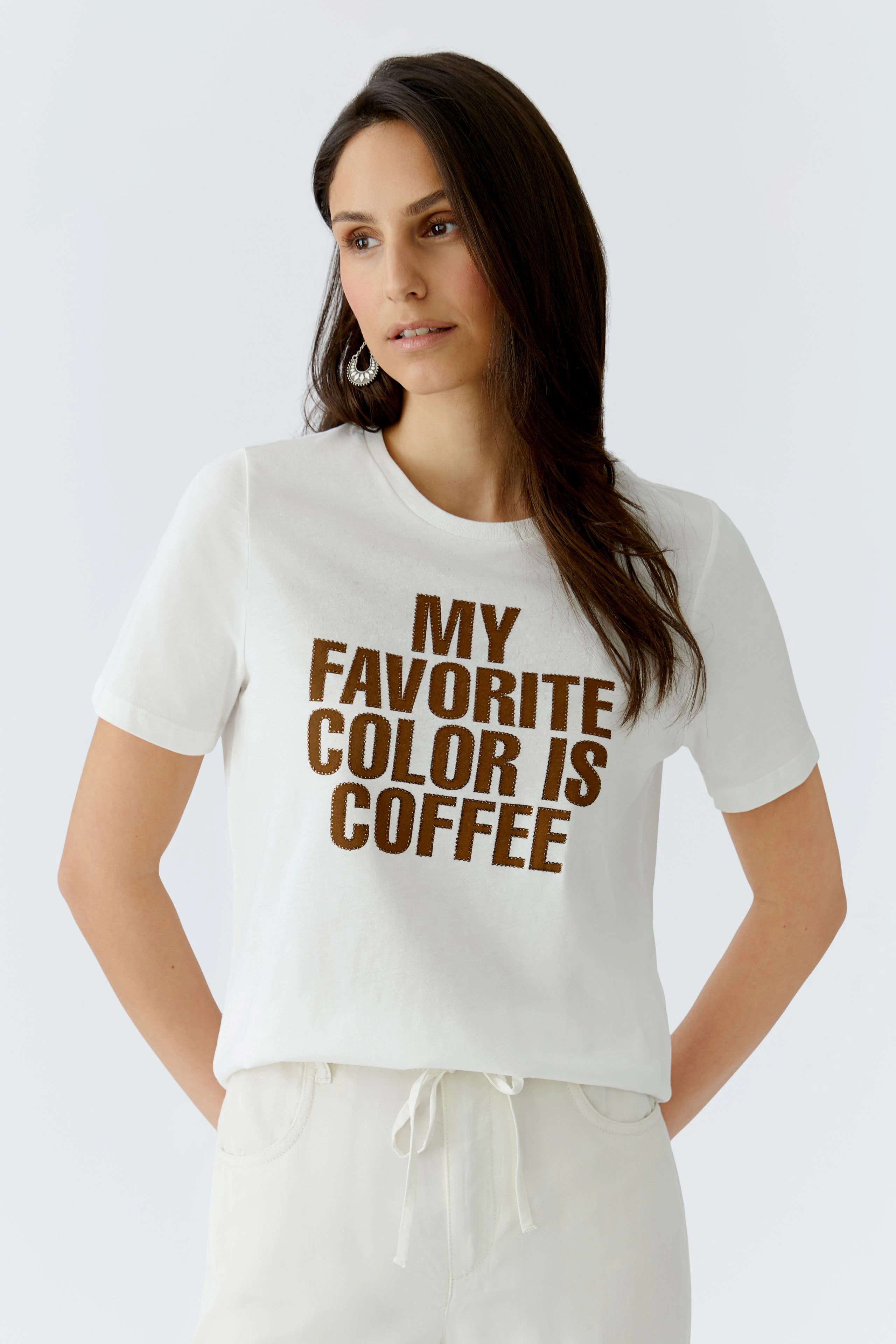Damen-T-Shirt: Junge Frau trägt ein weißes T-Shirt mit braunem Schriftzug 'MY FAVORITE COLOR IS COFFEE'.