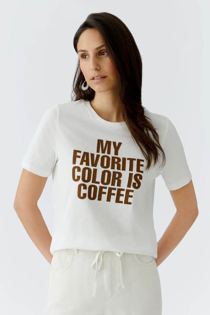 Casual women's T-shirt: Woman in a white tee with brown lettering saying 'MY FAVORITE COLOR IS COFFEE'.