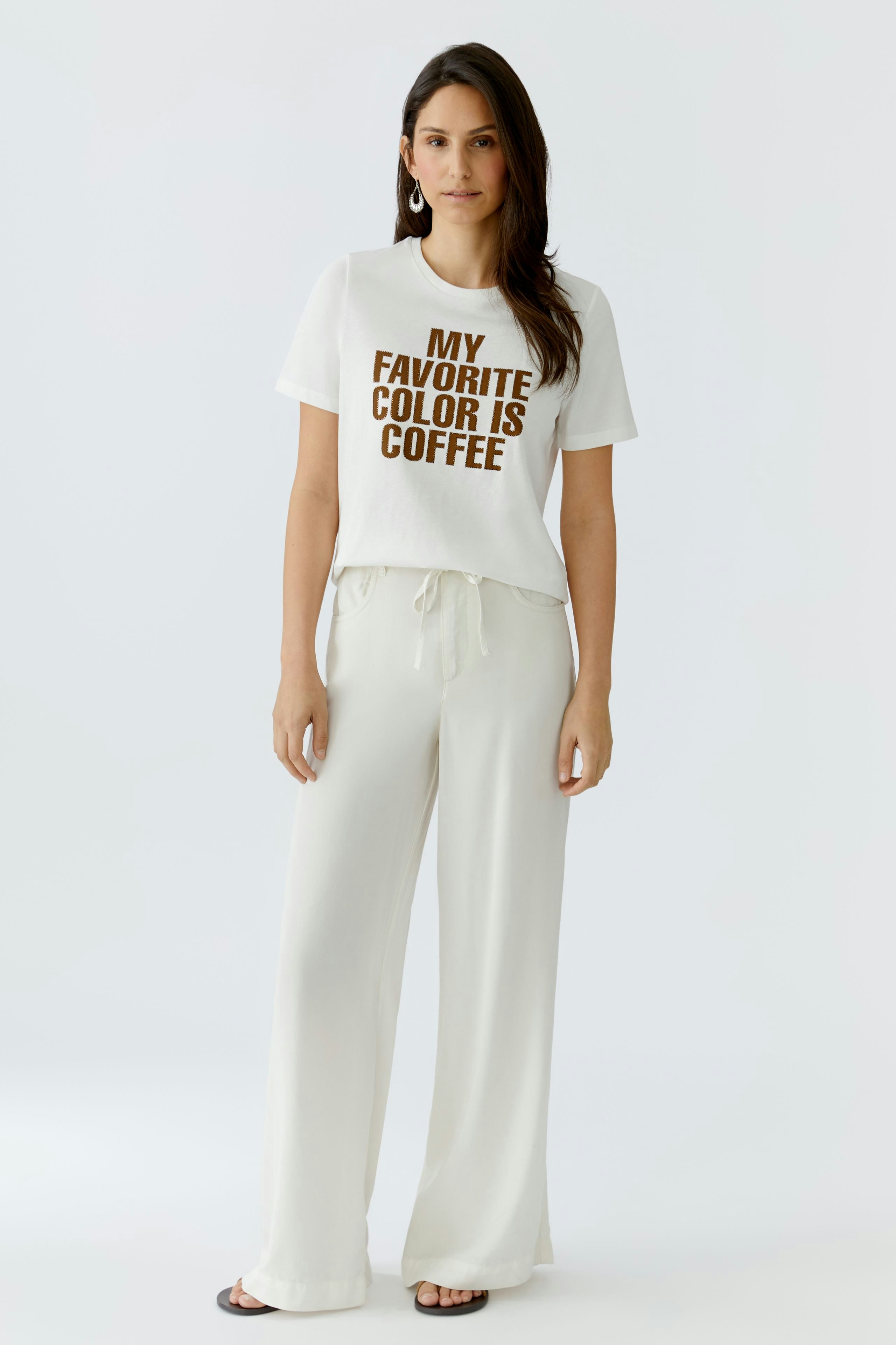 Damen-T-Shirt: Junge Frau trägt ein weißes T-Shirt mit braunem Aufdruck "MY FAVORITE COLOR IS COFFEE".