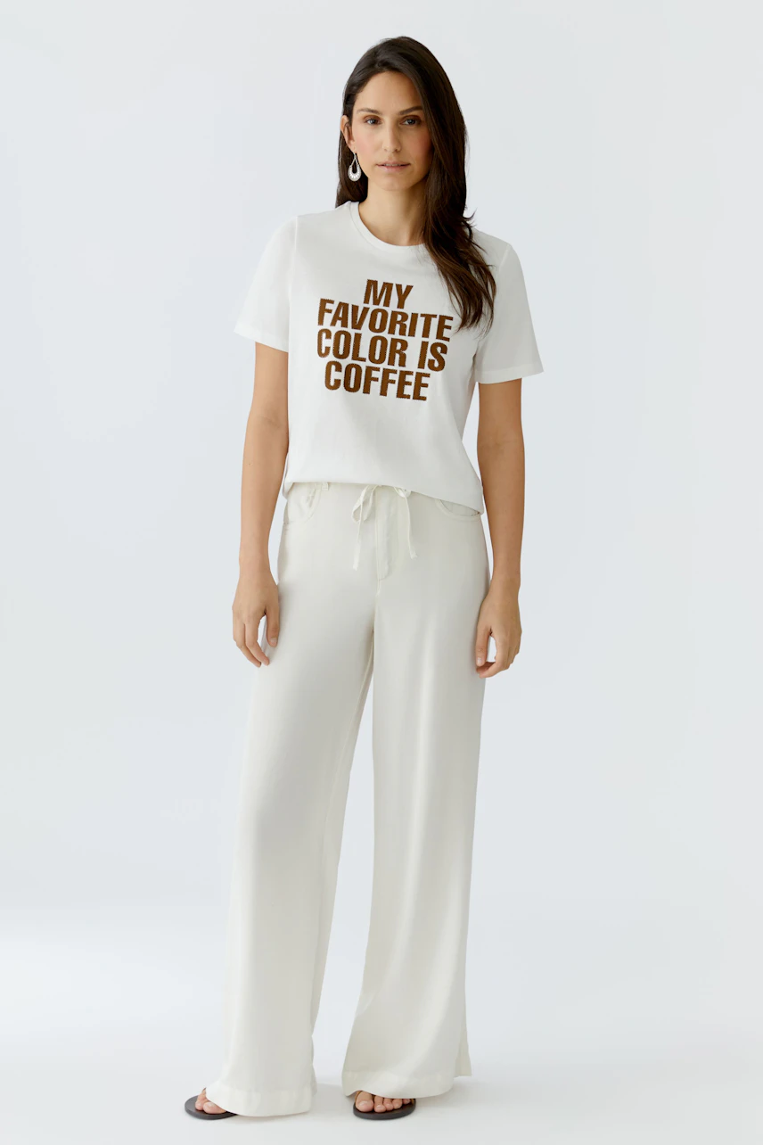 Casual women's T-shirt: Woman in a white tee with 'My favorite color is coffee' print, paired with light pants.