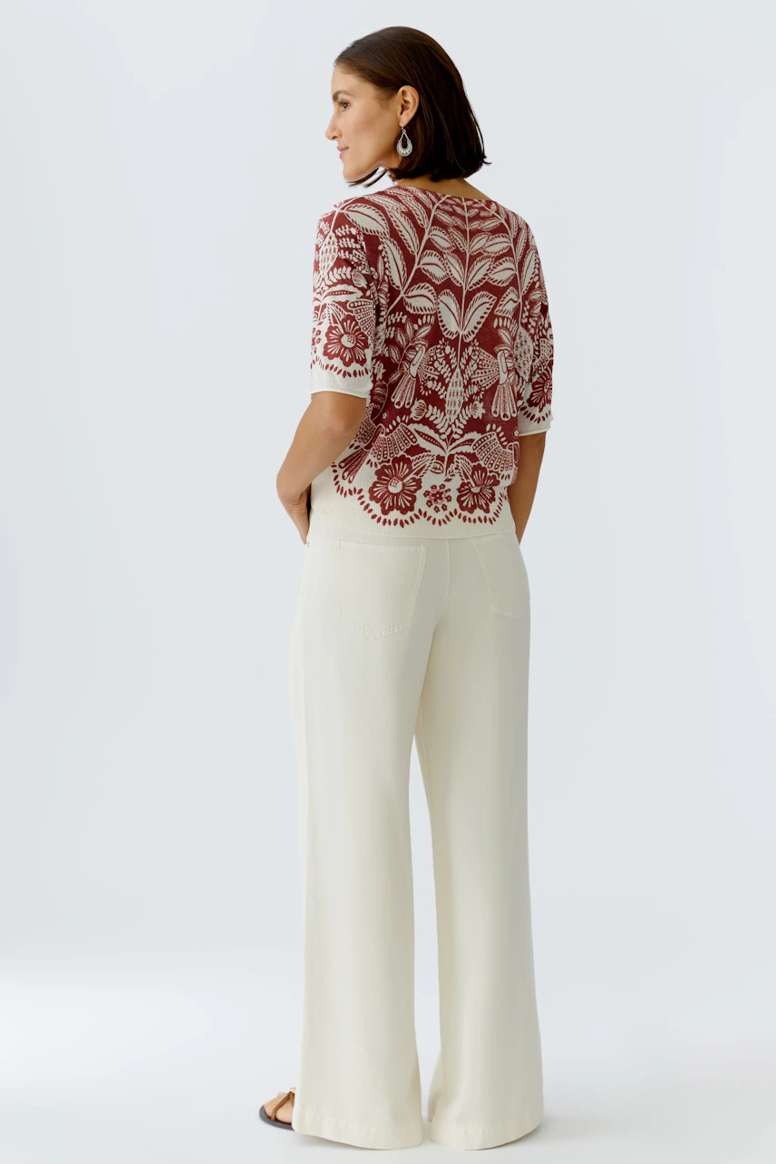 Casual women's pullover: A woman in a red floral pullover with a relaxed fit, paired with light trousers.
