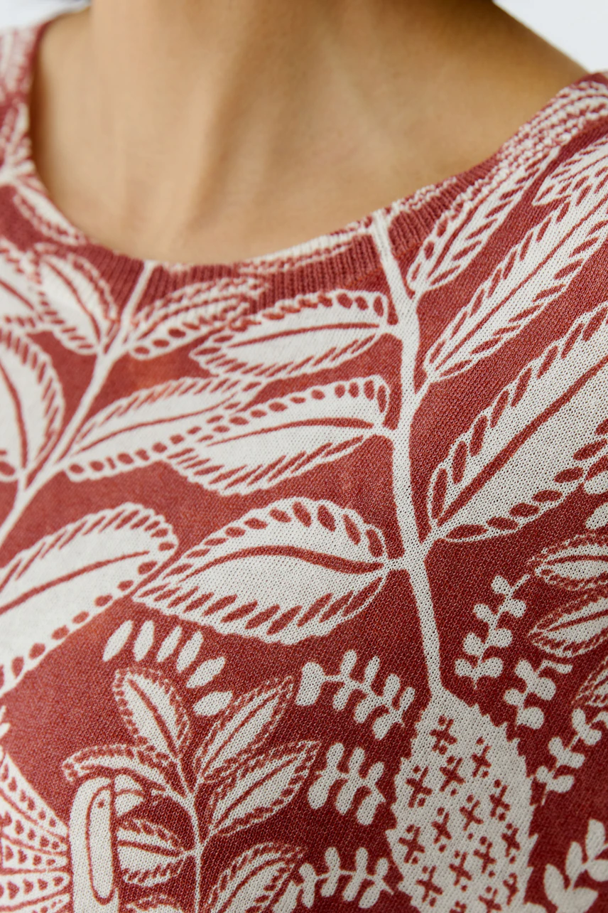 Casual women's pullover: Close-up of a woman wearing a red pullover with a leaf pattern.