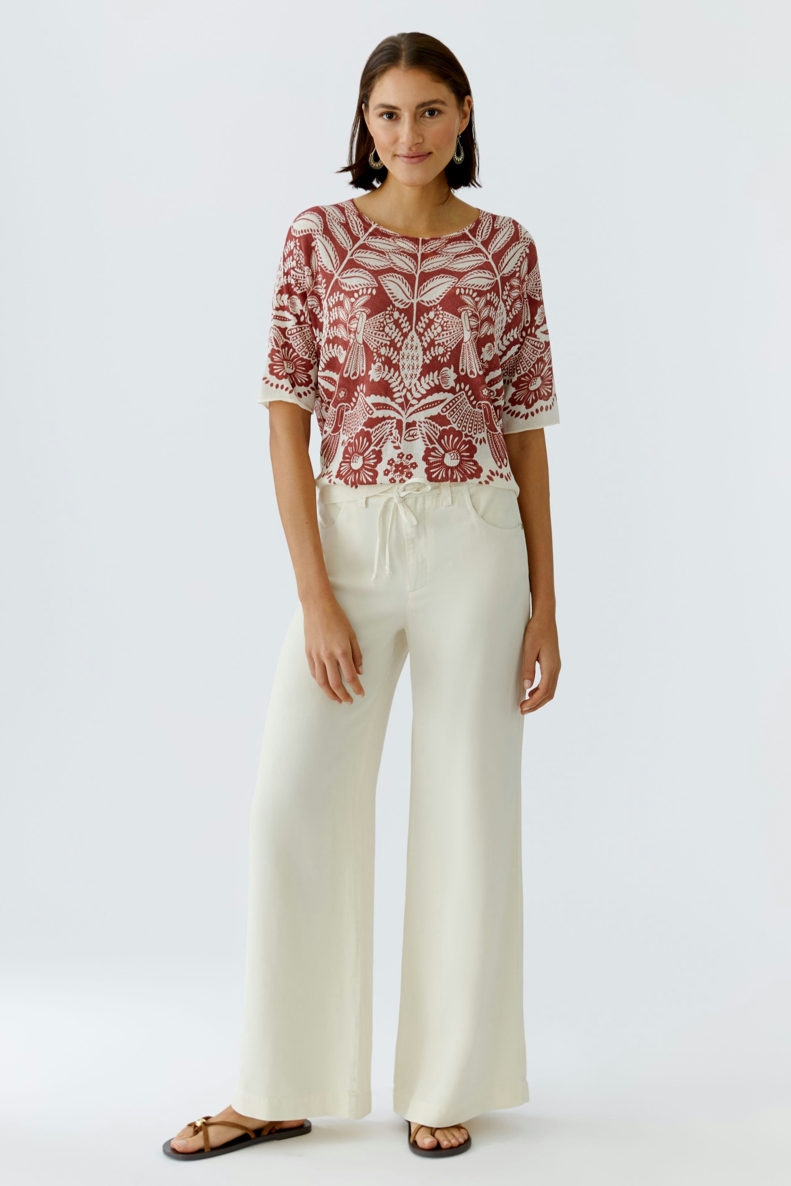 Damen-Pullover: Junge Frau in rotem, gemustertem Pullover mit lässigem Schnitt und weiten Hosen.