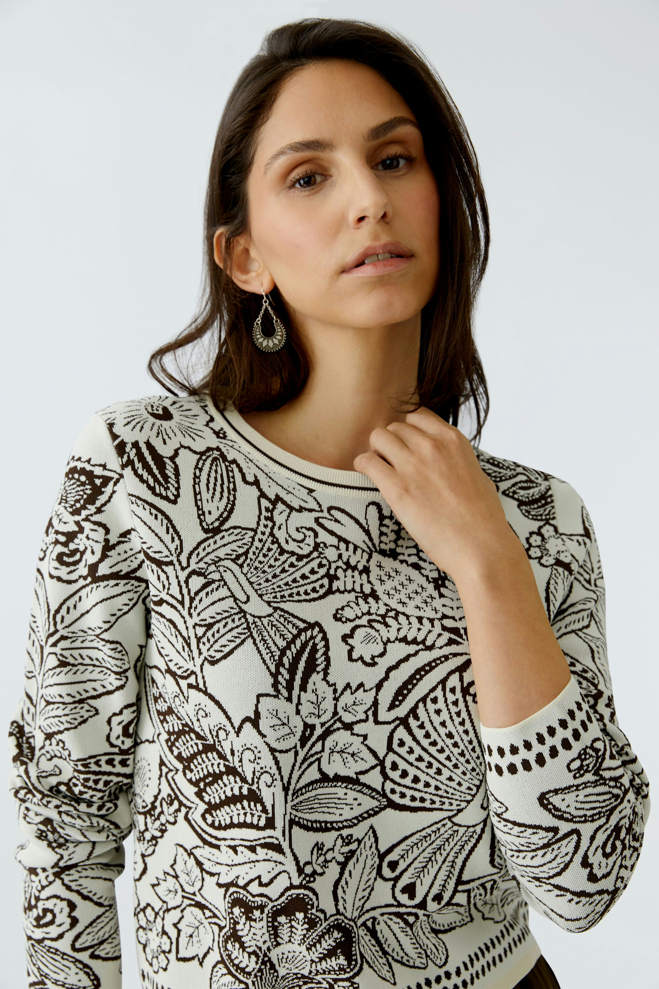 Damen-Pullover: Frau trägt einen gemusterten Pullover mit floralen Motiven und lässigem Schnitt.