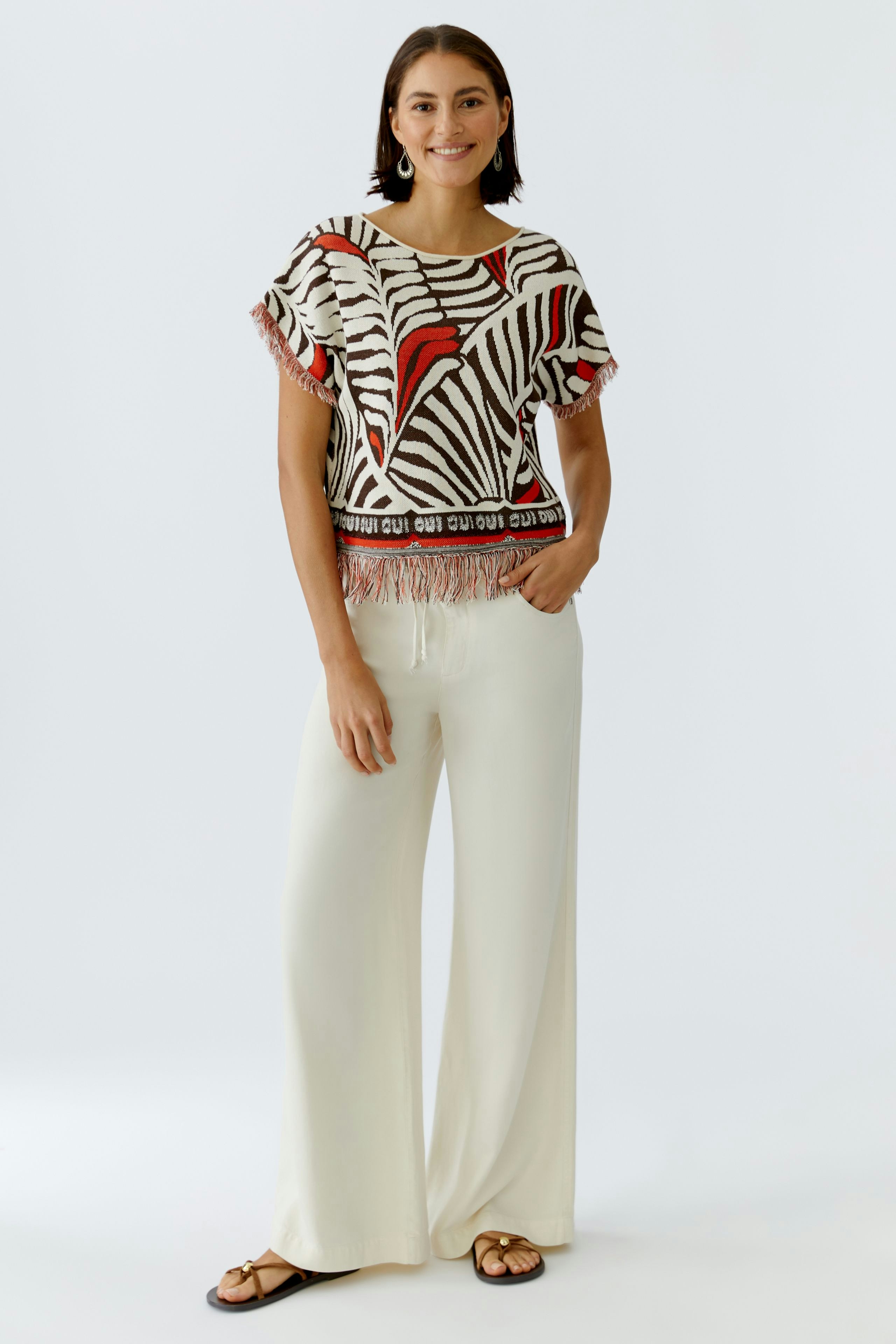 Damen-Pullover: Junge Frau trägt einen gestreiften Pullover mit Fransen und lässigen, hellen Hosen.