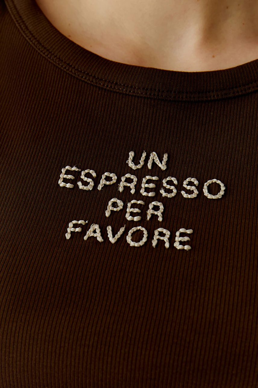 Casual women's tank top: Close-up of a woman wearing a brown ribbed tank top with embroidered text.