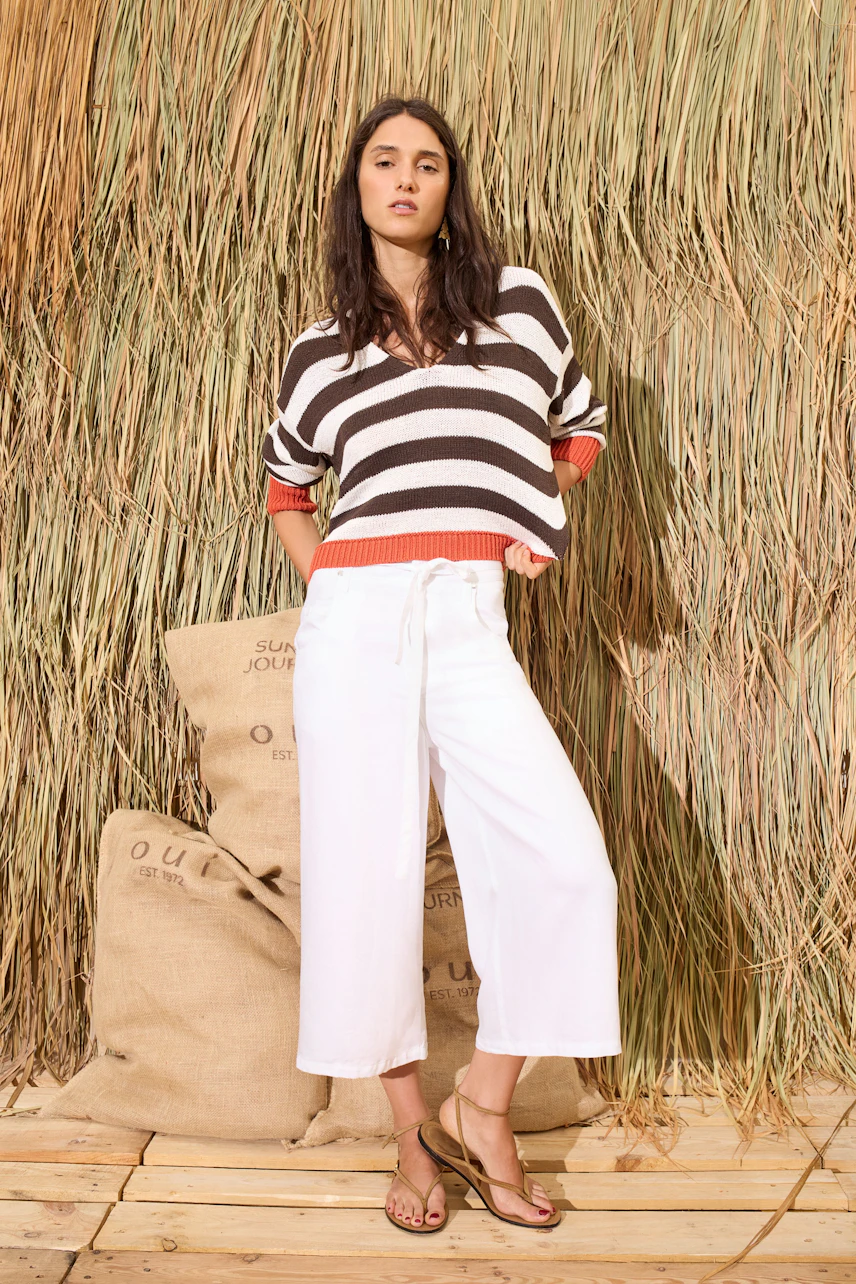 Casual women's pants: Woman in white wide-leg pants with a striped pullover stands confidently.