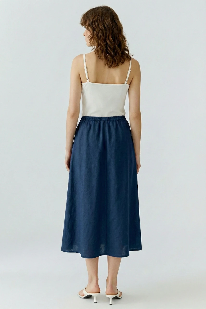 A-line skirt: Woman in a white top and blue A-line skirt, standing with her back to the camera.