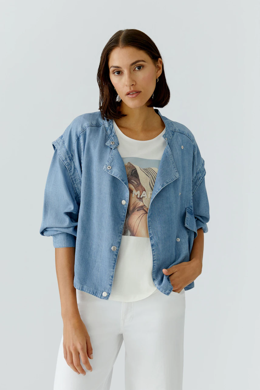 Casual women's denim jacket: A woman in a light blue jacket over a graphic tee, paired with white pants.