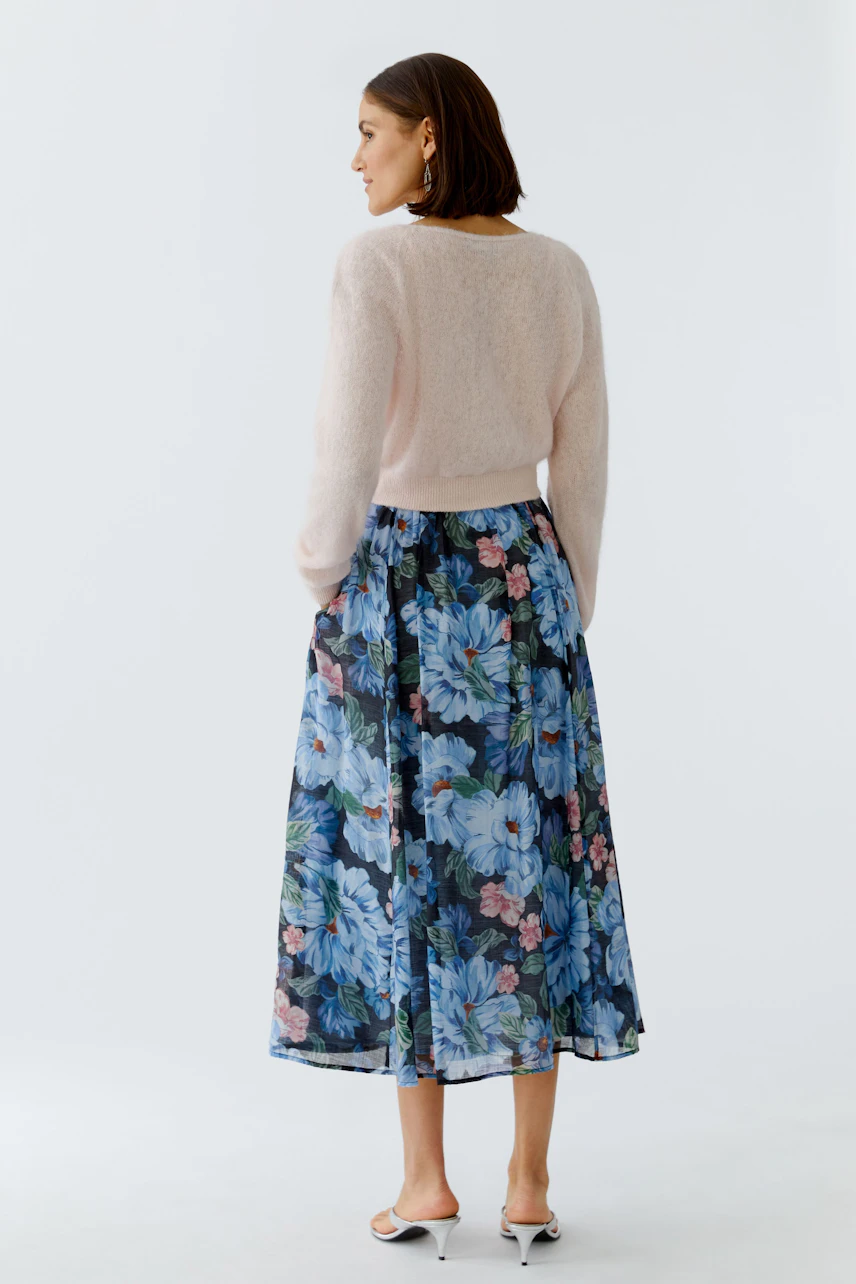 Soft women's cardigan in light pink, paired with a floral skirt, showcasing a relaxed style.