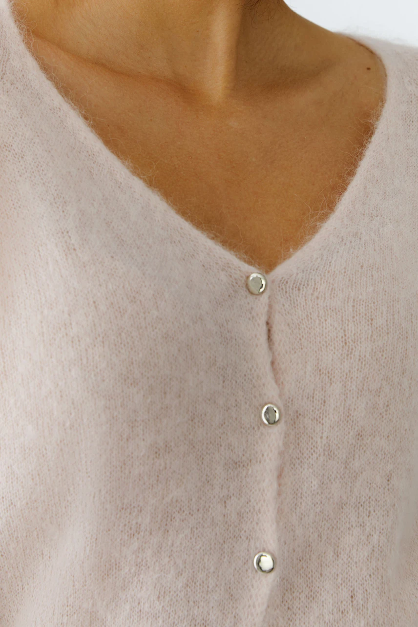 Soft pink cardigan with a V-neck and silver buttons, worn by a woman.