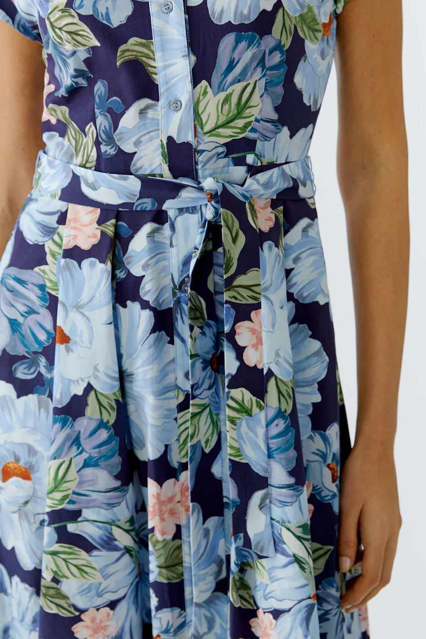 Floral midi dress: Woman in a blue floral dress with a button-up front and a tied waist.