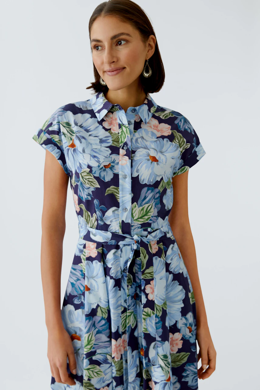 Floral mididress: Woman in a blue floral dress with short sleeves and a tied waist, smiling softly.