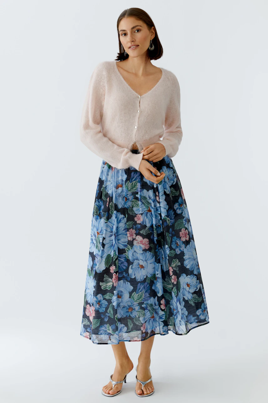 Floral pleated skirt: Woman in a light pink cardigan and a long skirt with vibrant flowers.