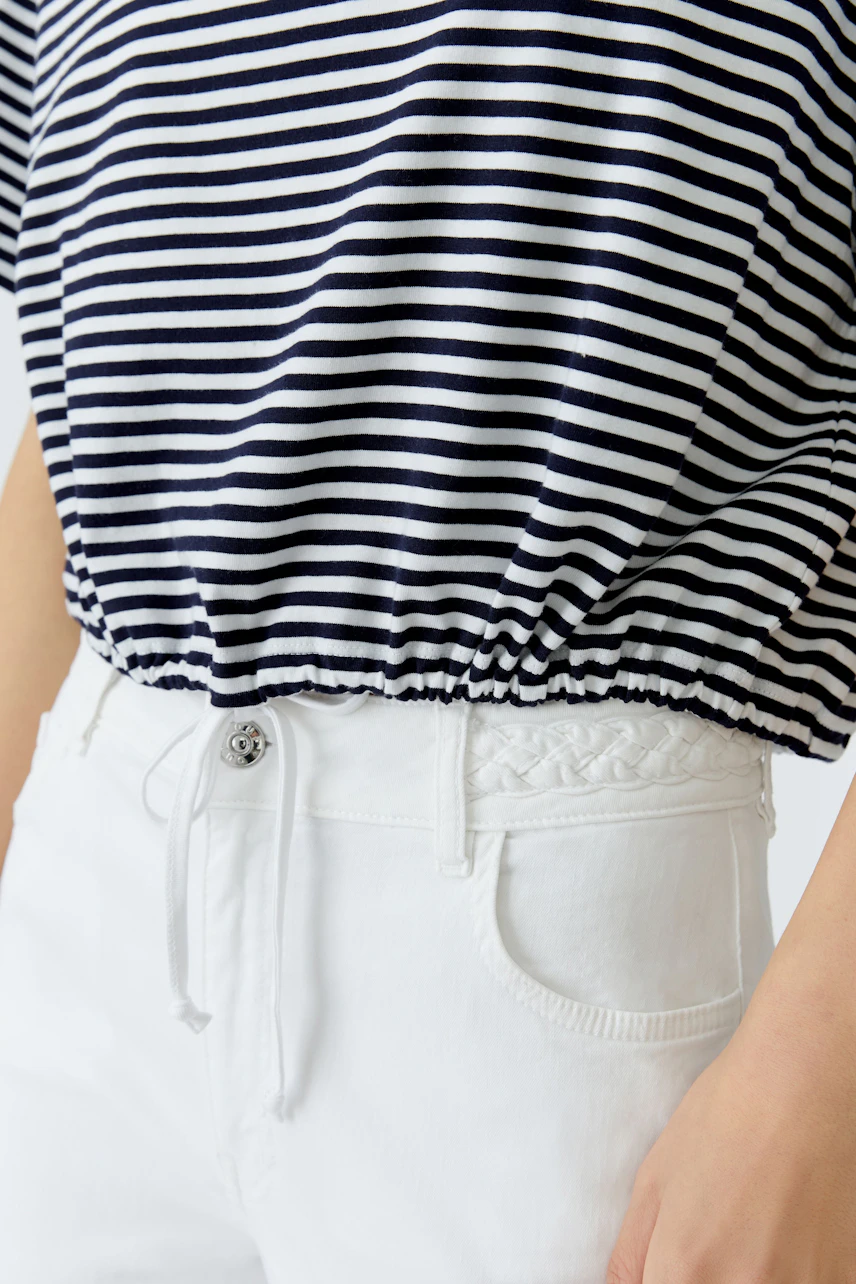 Casual women's polo shirt: A woman in a striped polo shirt with a gathered hem, paired with white pants.