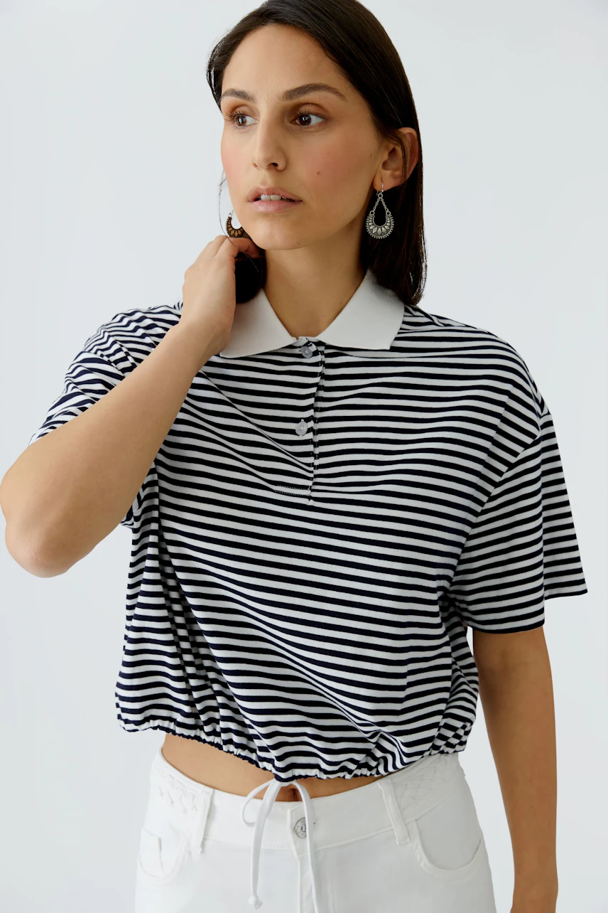 Casual women's polo shirt: A woman in a striped polo with a drawstring hem, styled with white pants.