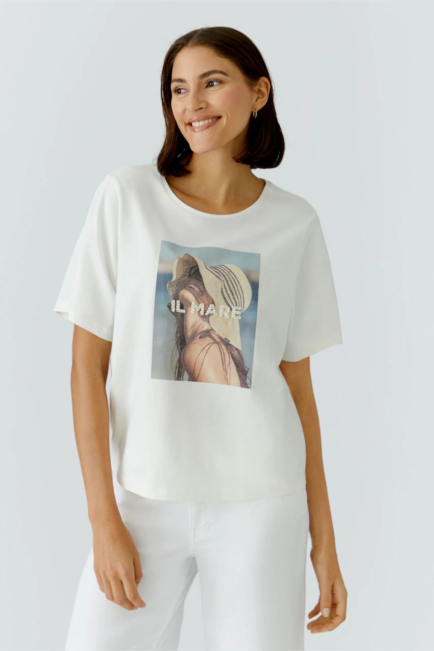 Casual women's T-shirt: Smiling woman in a white tee with a beach graphic, paired with light pants.