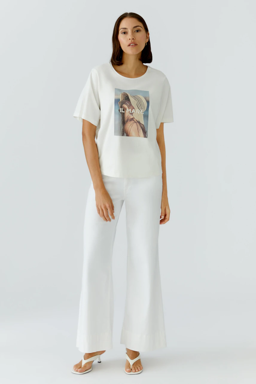 Casual women's T-shirt: Woman in a light top with a graphic print, paired with wide white pants.
