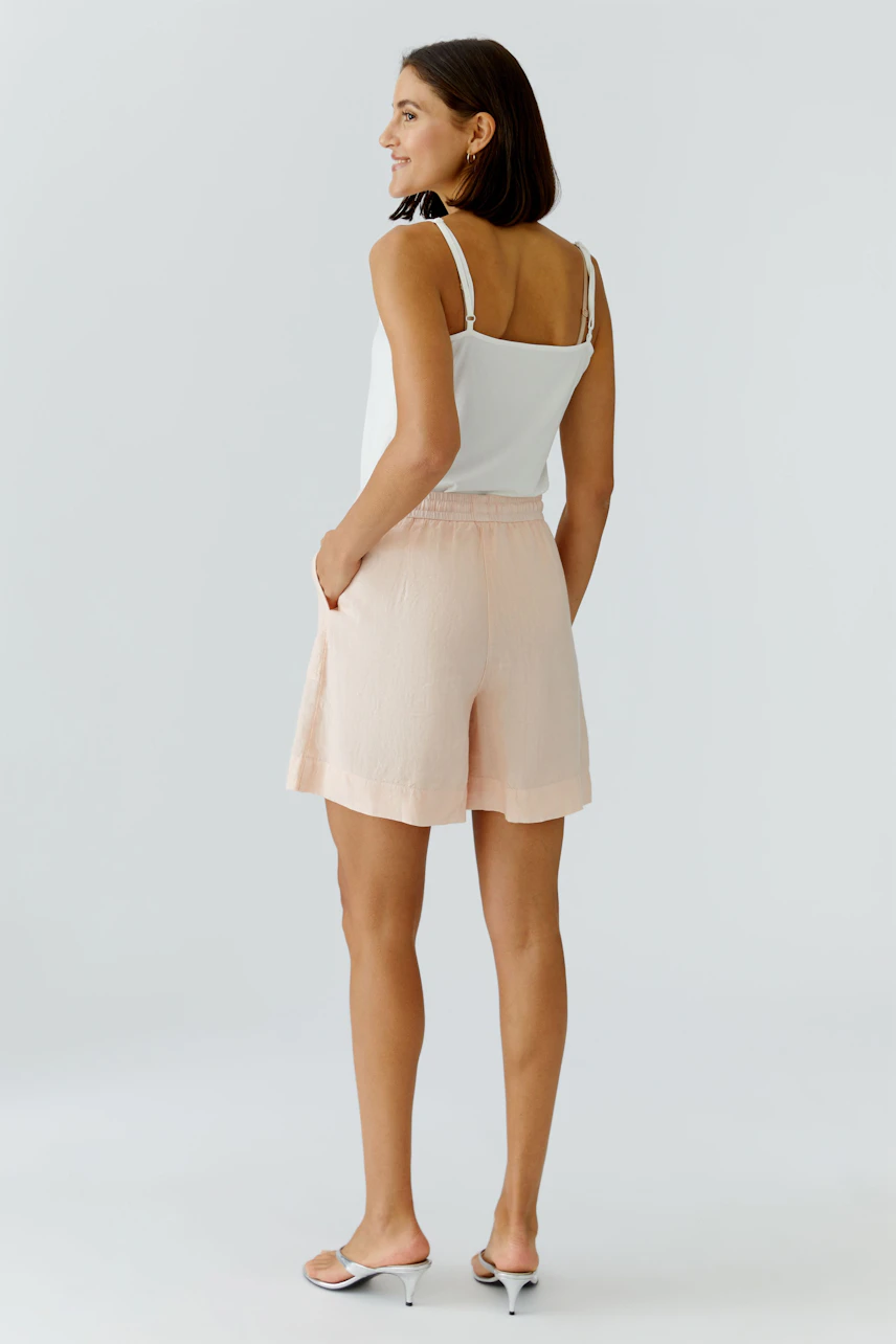 Casual women's shorts: A woman in light pink shorts and a white tank top stands confidently.