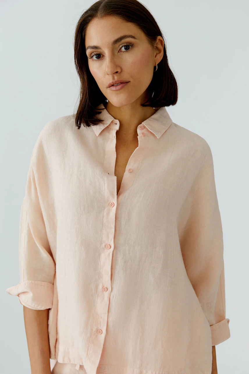 Casual women's blouse: A woman in a light pink button-up blouse with rolled sleeves, looking relaxed.